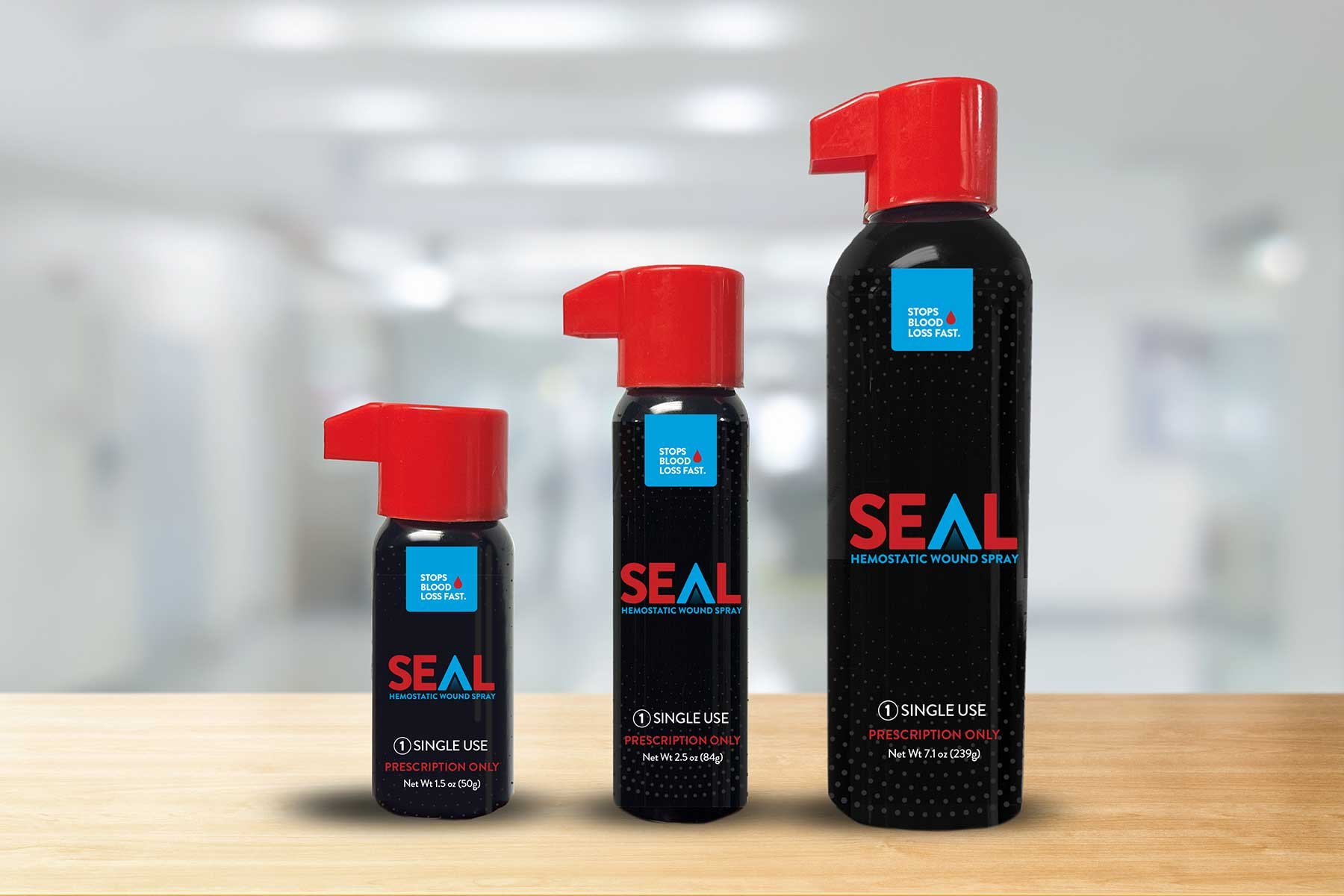 Three bottles of SEAL hemostatic wound spray in different sizes on a wooden surface, with white and blurred background.