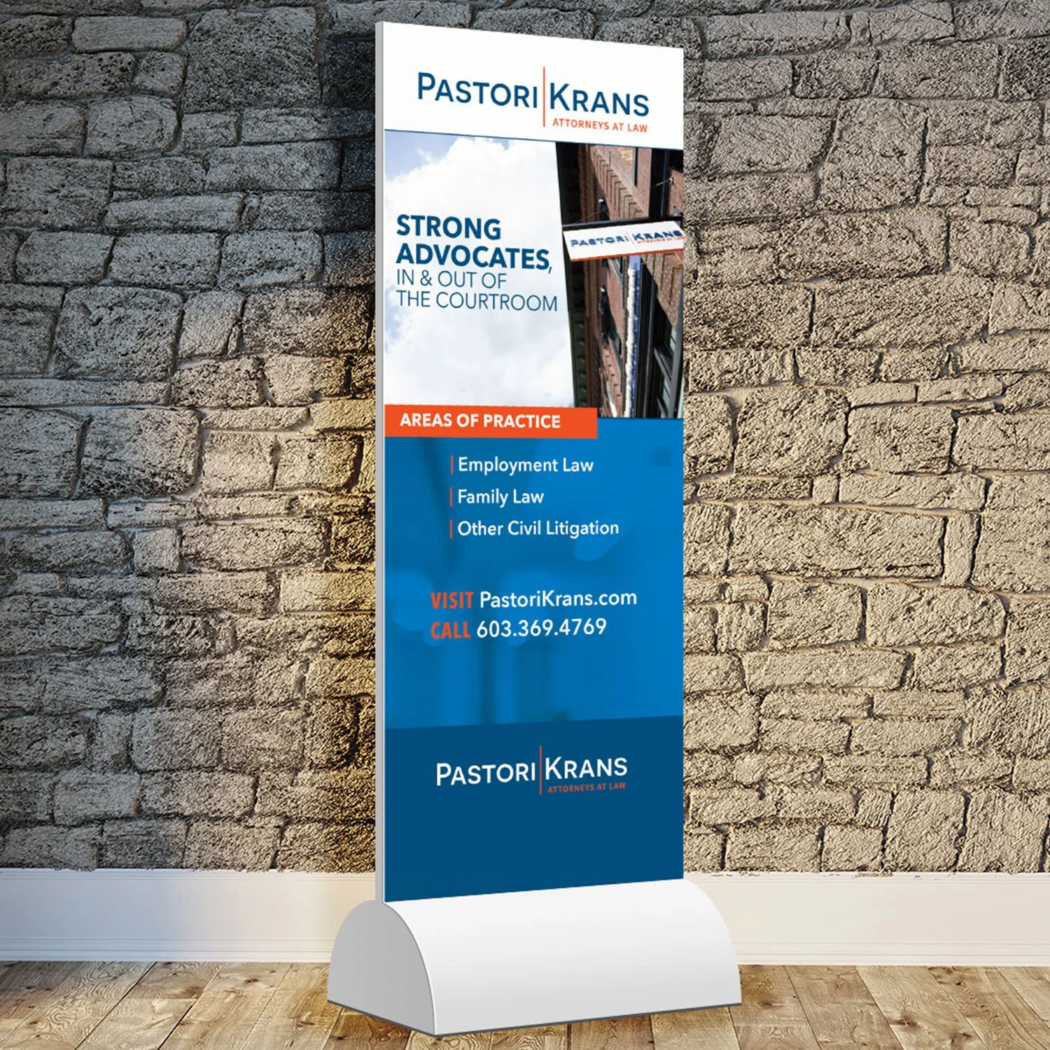 A vertical banner advertisement for Pastori Krans, attorneys at law, placed against a brick wall. The banner promotes strong advocates in and out of the courtroom and lists practice areas including employment law, family law, and civil litigation. It