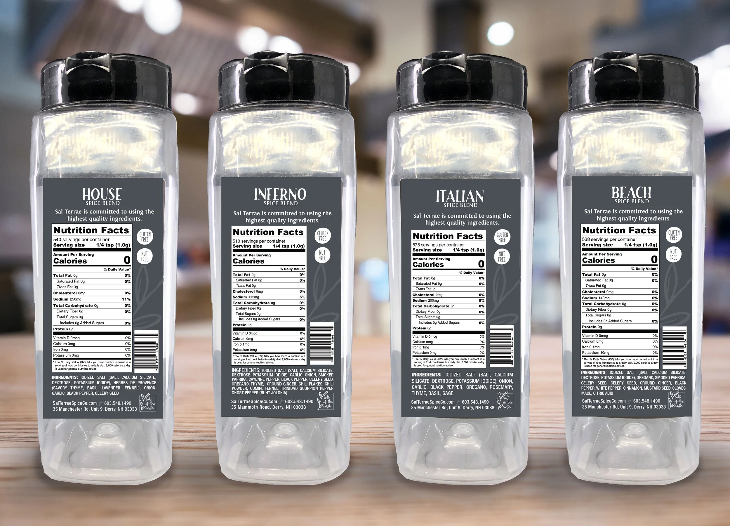 Four clear plastic spice jars with black lids, labeled 'House,' 'Inferno,' 'Italian,' and 'Beach,' placed on a wooden surface against a blurred background of a kitchen or pantry.