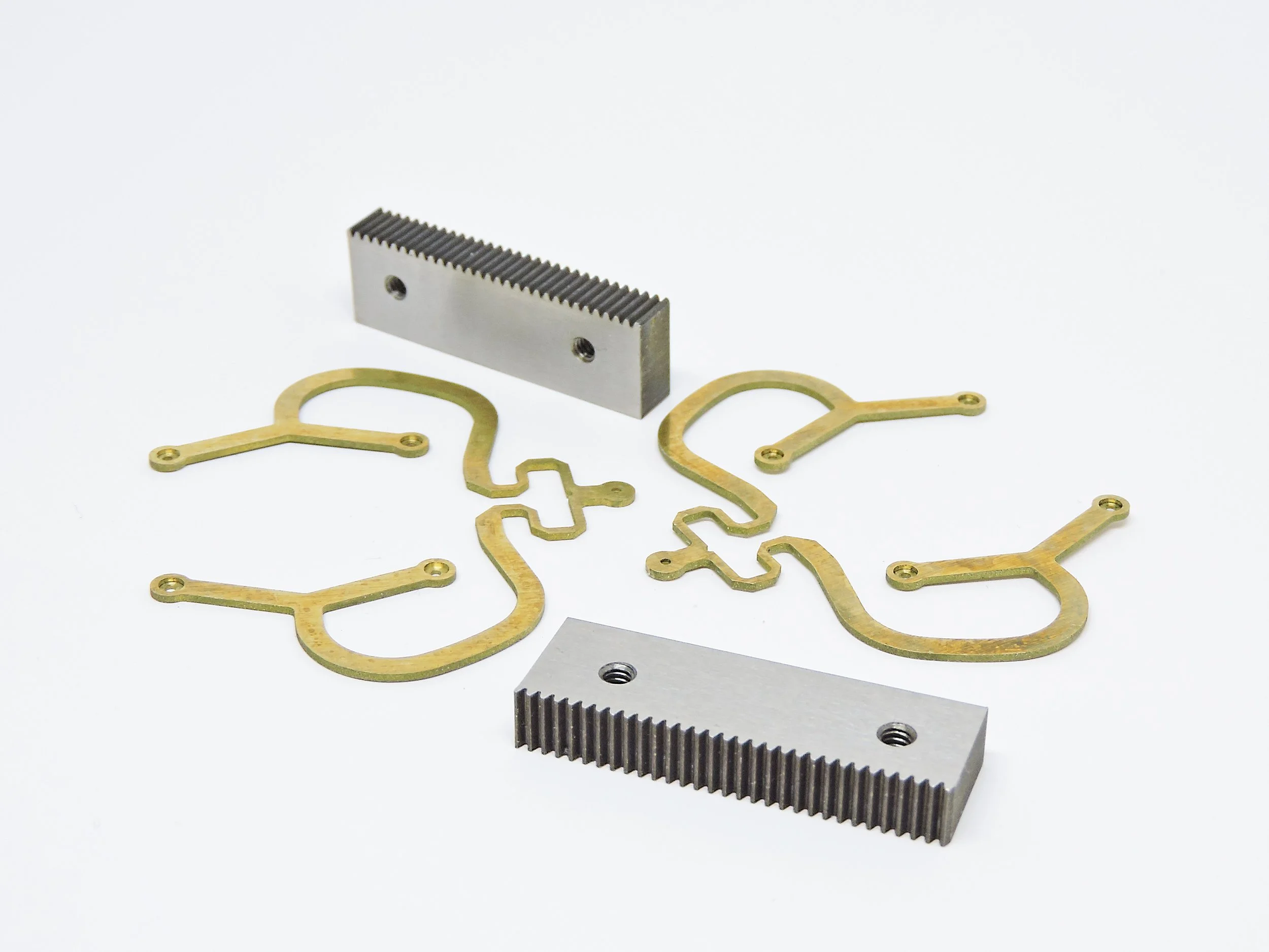 Disassembled mechanical parts including two metal gear racks and several gold-colored brackets or spacers, arranged on a white background.