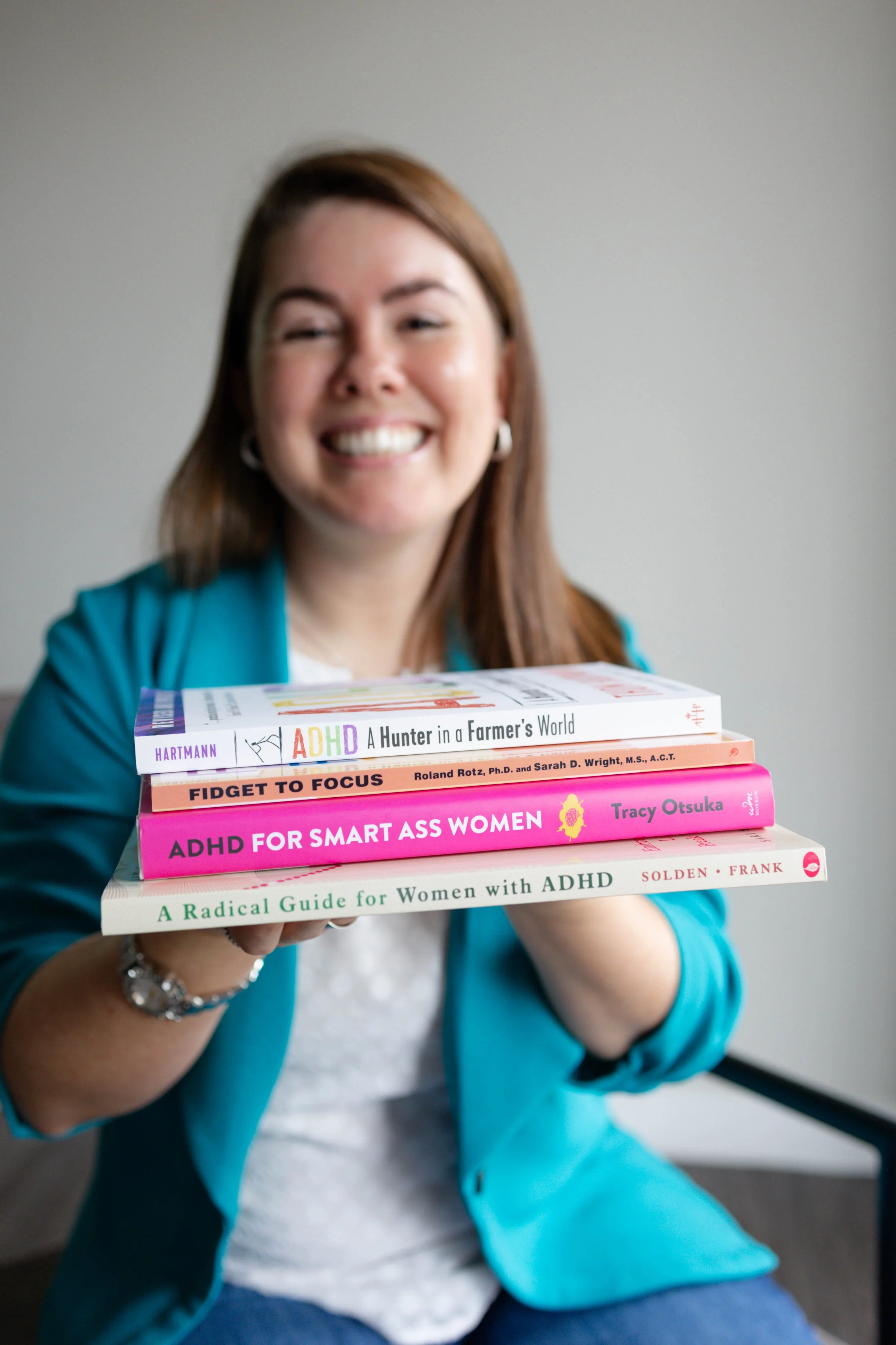 A woman smiling and holding a stack of four books about ADHD.