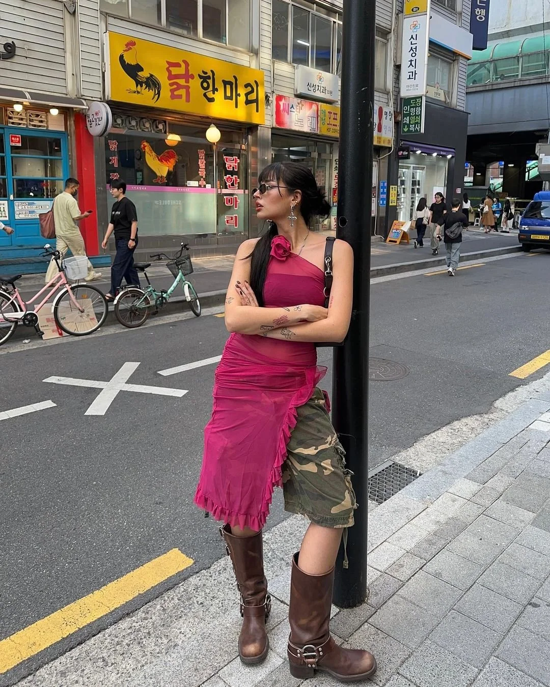 Woman in pink outfit leaning on a pole in an urban setting with a chicken restaurant in the background.