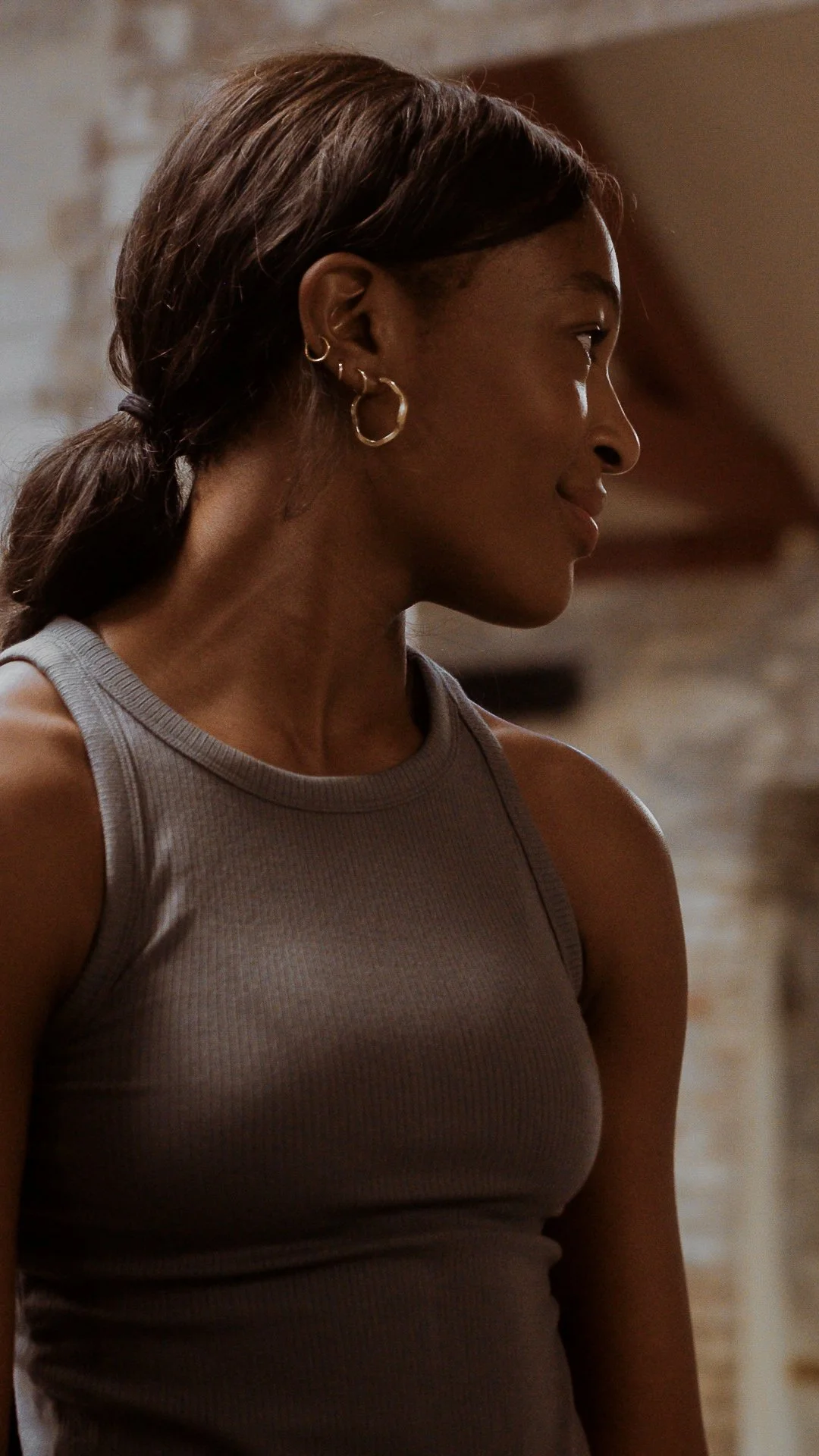 Woman in a gray tank top with hoop earrings, side profile view