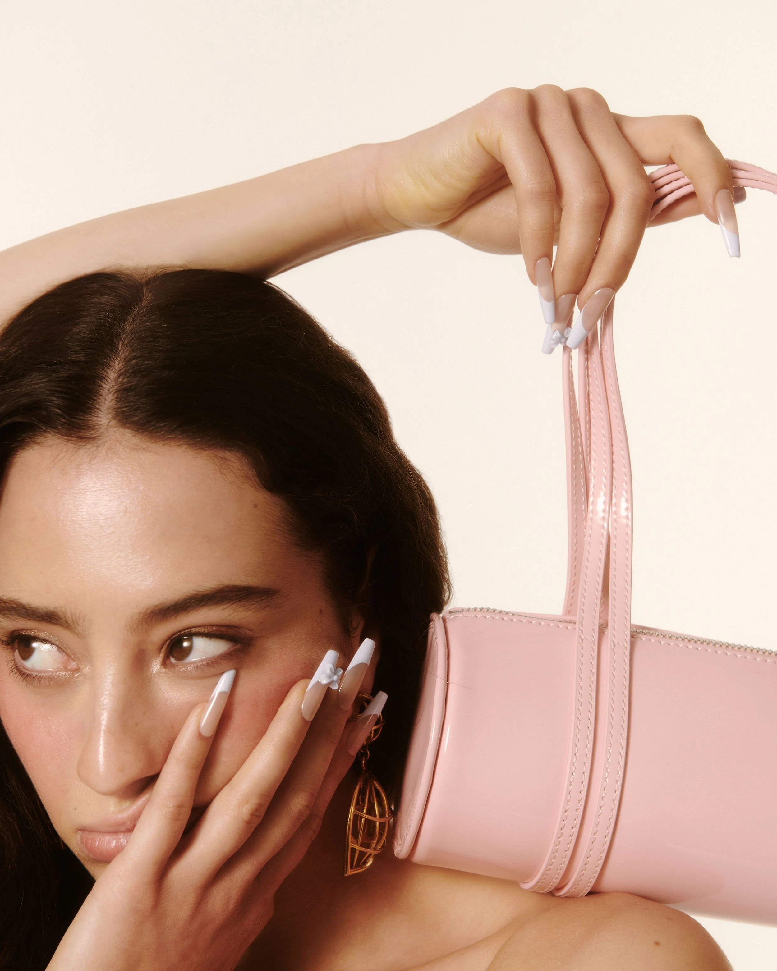 Person with long decorated nails holding a pink handbag on their shoulder.