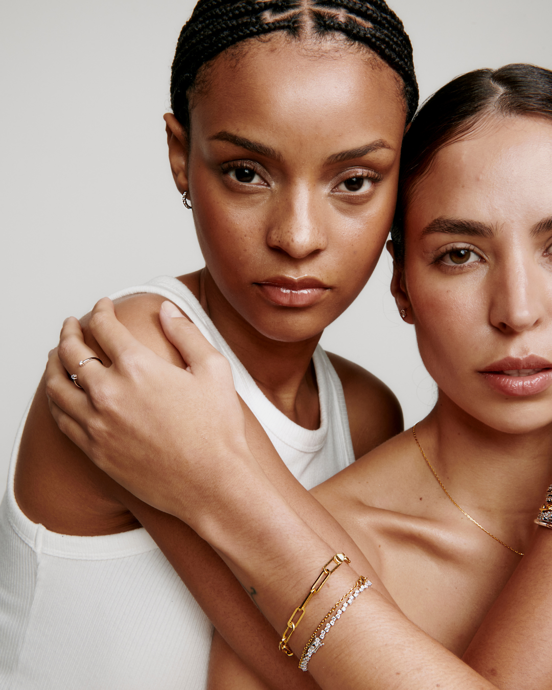 Two women posing closely, wearing gold jewelry and casual tops.