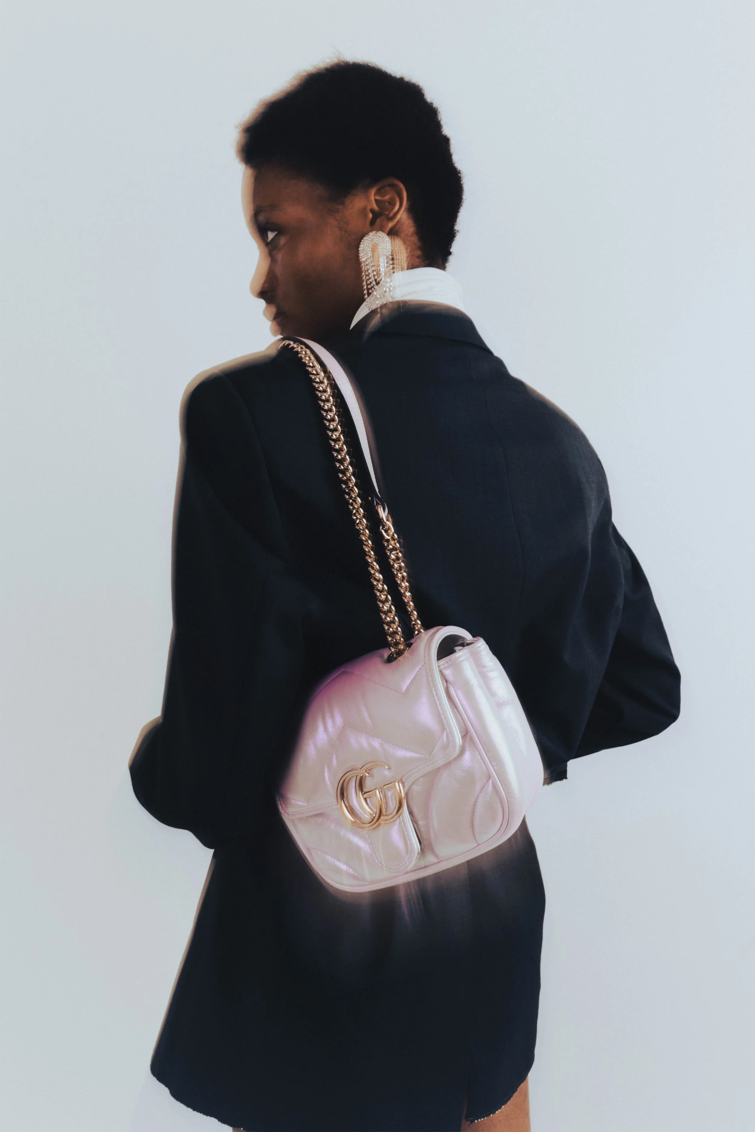 Person wearing a black blazer, large earrings, and a pink Gucci handbag with a gold chain strap.