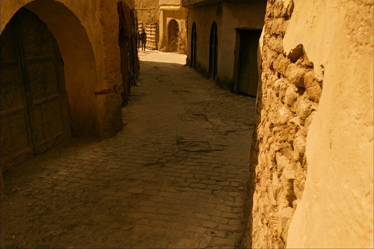 A narrow cobbled medina lane in Fes with uneven worn paving stones