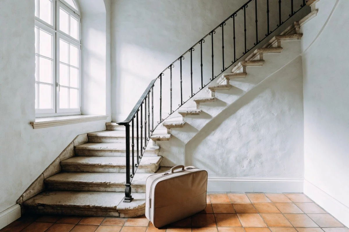 A single packed suitcase at the foot of a stone staircase in an old hotel with no elevator