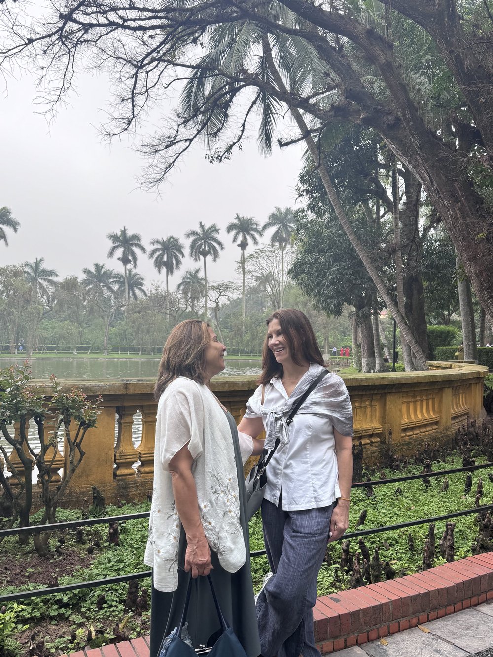 Two Dandelion Journals travelers smiling beside a yellow stone railing by a pond in Vietnam