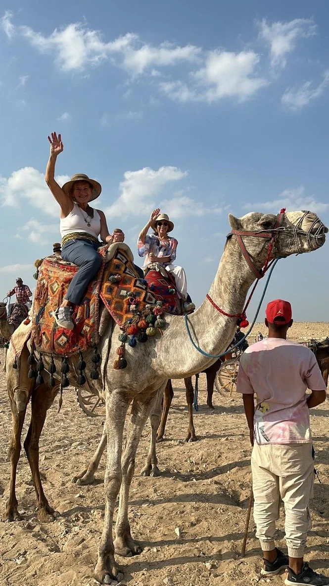 Travelers riding camels across the sand beside the pyramids