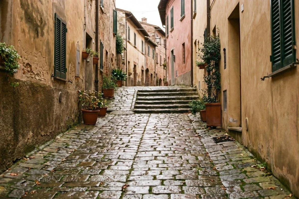 A wet cobblestone lane rising through a Tuscan hill town in autumn