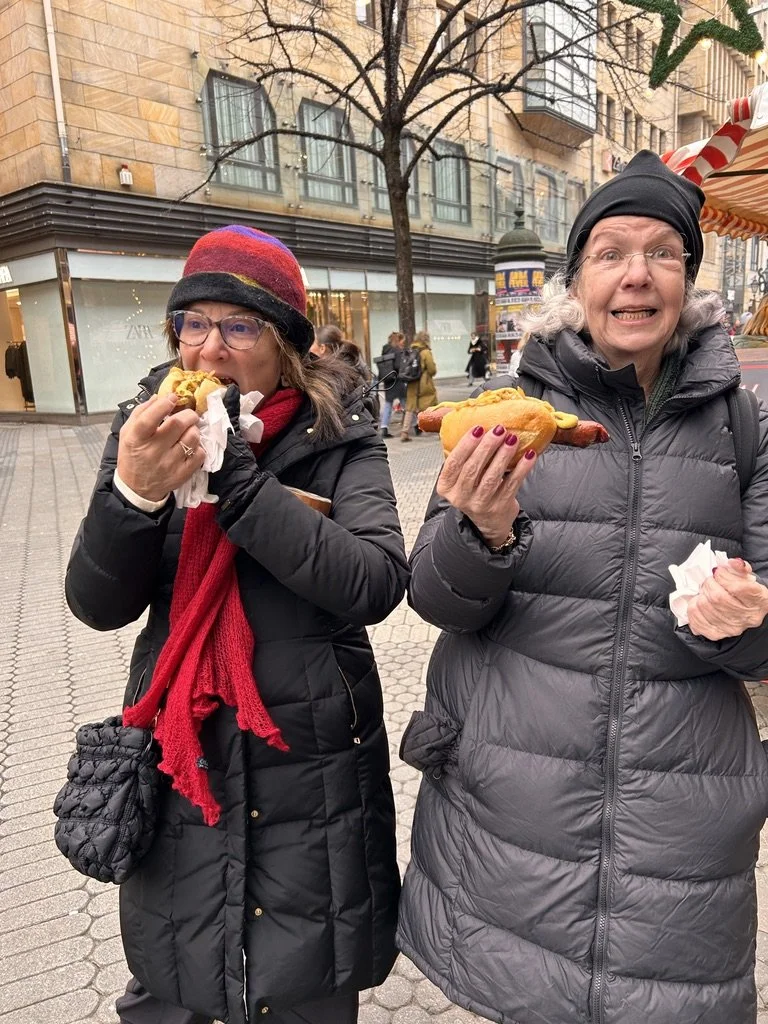 Two travelers bundled in winter coats holding hot drinks at a German Christmas market