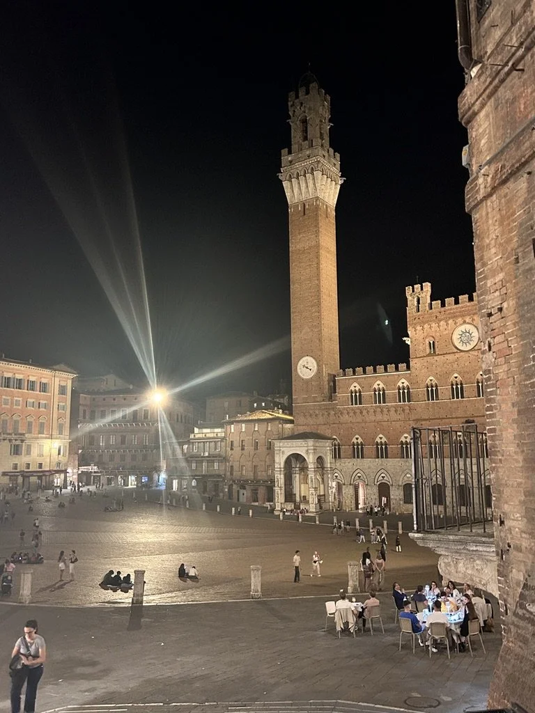 A medieval Tuscan piazza and tower glowing at night