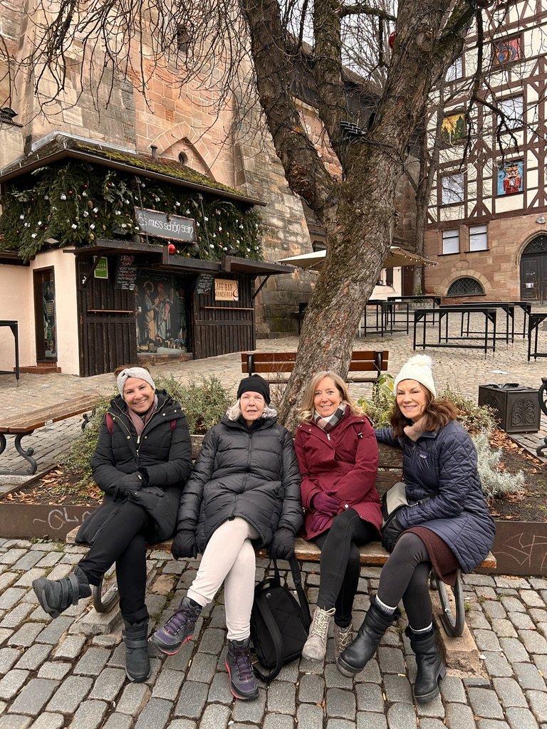 Four women bundled in winter coats and hats sitting together on a bench in Germany