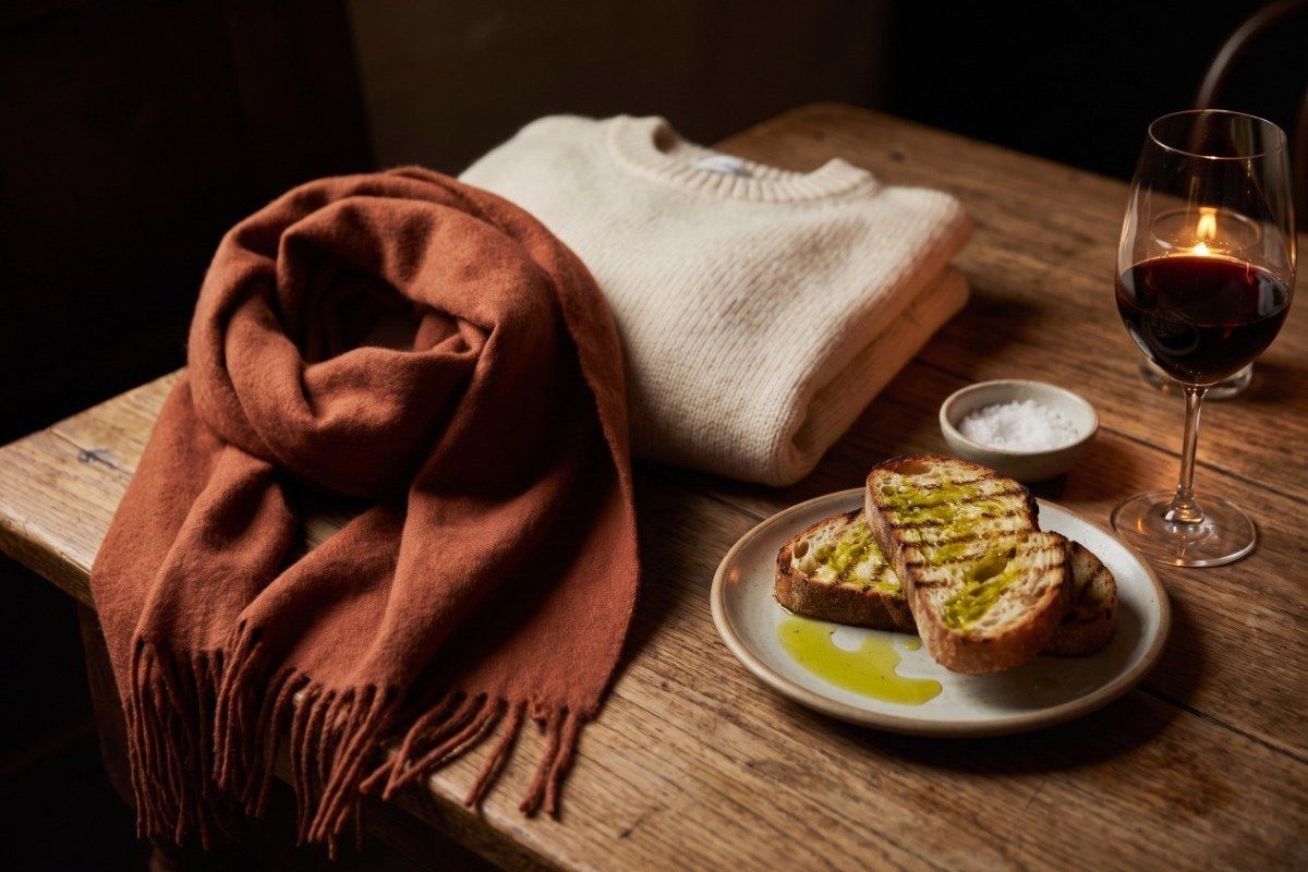 A rust wool scarf and cream sweater beside grilled bread with new-pressed olive oil