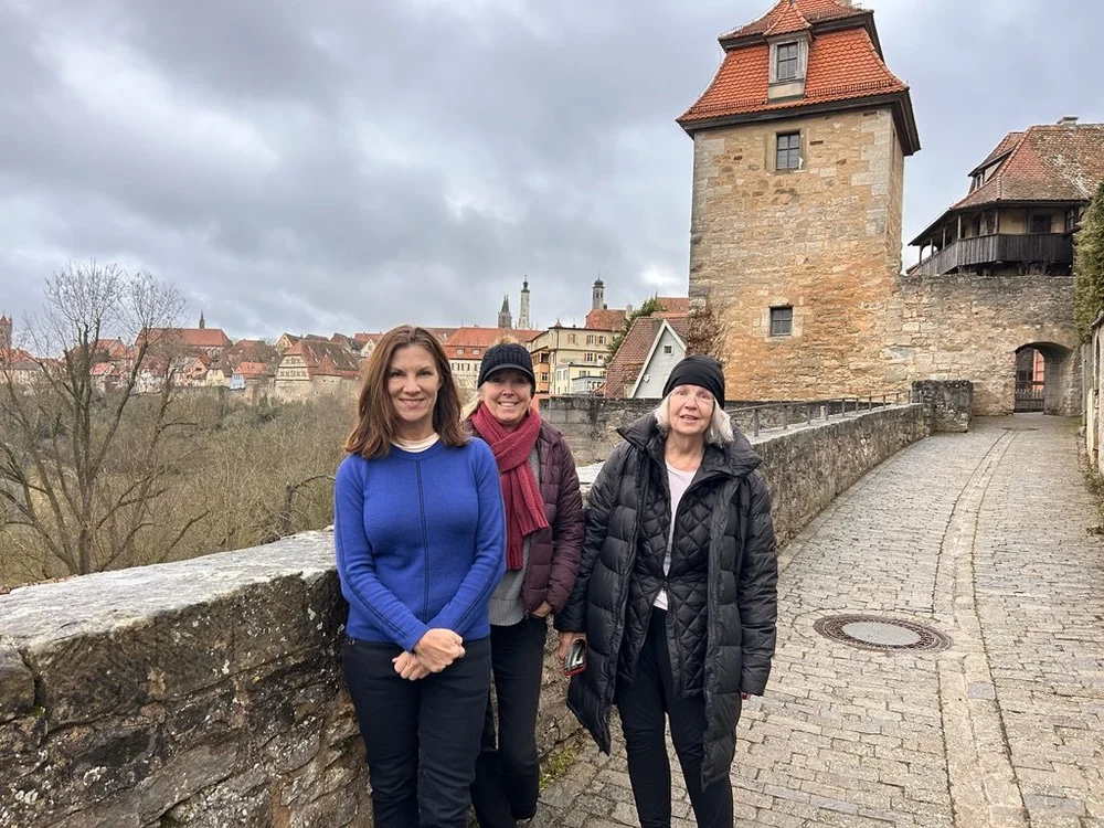 Three travelers walking a cobblestone path beside a stone castle wall and tower