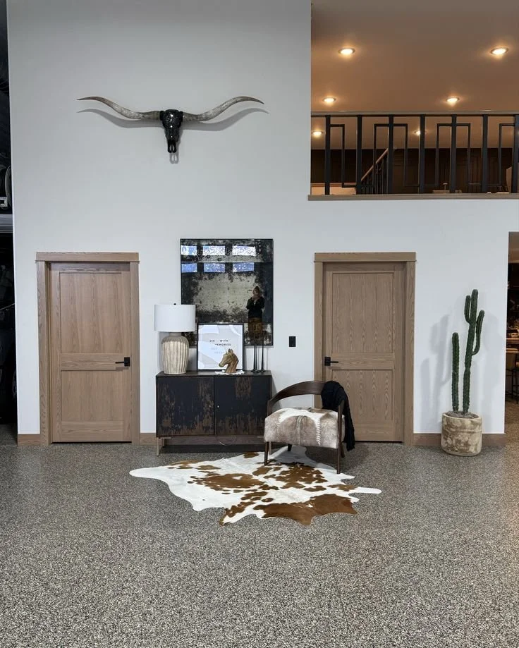 Interior space with two wooden doors, a wall-mounted longhorn skull, a console table with a lamp and decorative items, a cowhide rug, a modern chair, and a potted cactus plant.