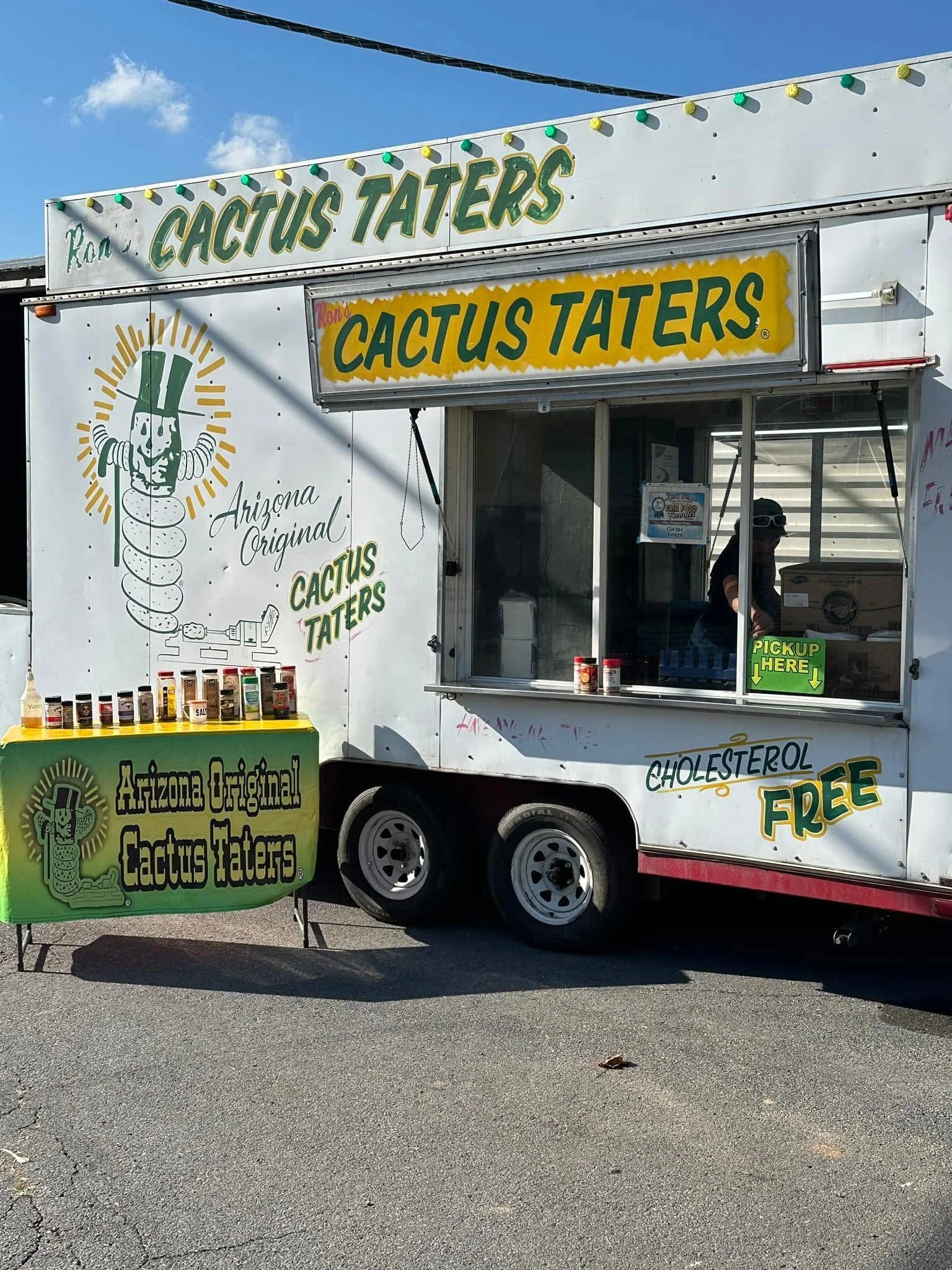 Food truck selling cactus Taters, with bottles of condiments on a green stand in front, under a blue sky.