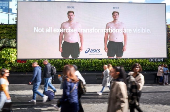 An outdoor digital billboard for ASICS featuring side-by-side "Before" and "After" photos of a man whose physical appearance has not changed. The text reads: "Not all exercise transformations are visible."