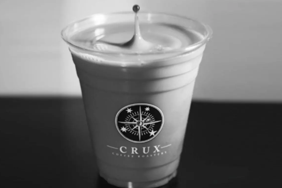 Plastic cup with logo on table, containing coffee with a swirl on top, monochrome.