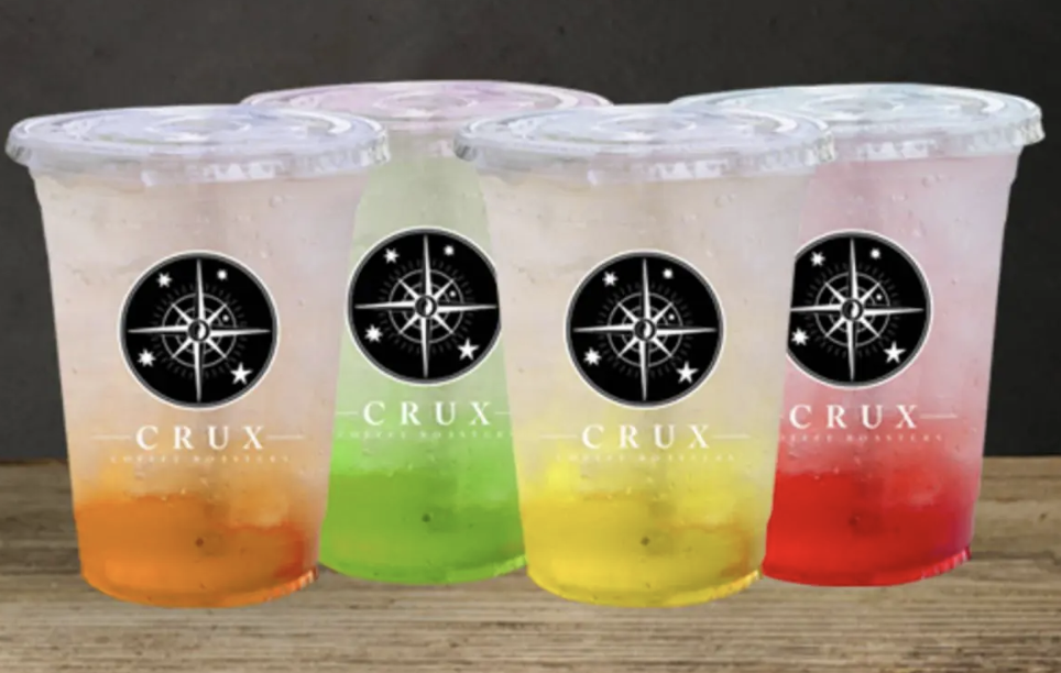 Four cups of colored iced beverages labeled Crux with compass star logo
