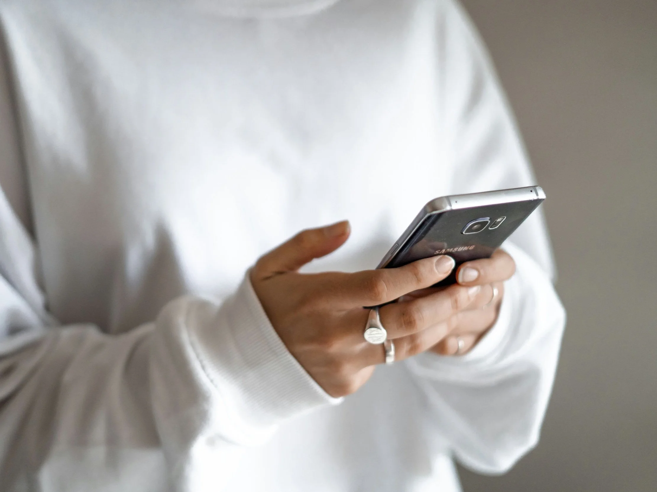 Person wearing a white long-sleeve shirt holding a Samsung smartphone with both hands.