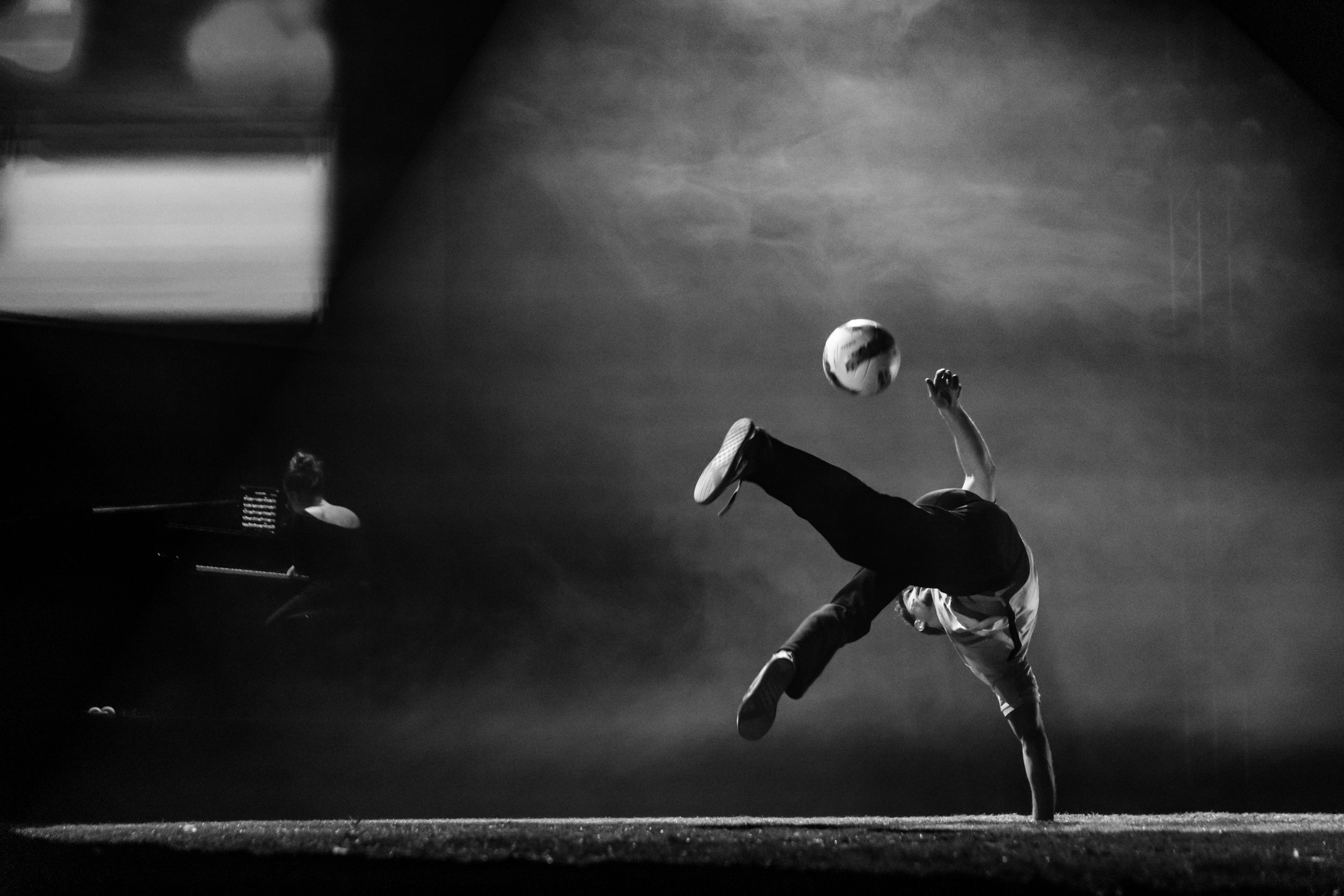 Un joueur de football effectue une acrobatie en dégagement lors d'un match, avec un piano en arrière-plan.
