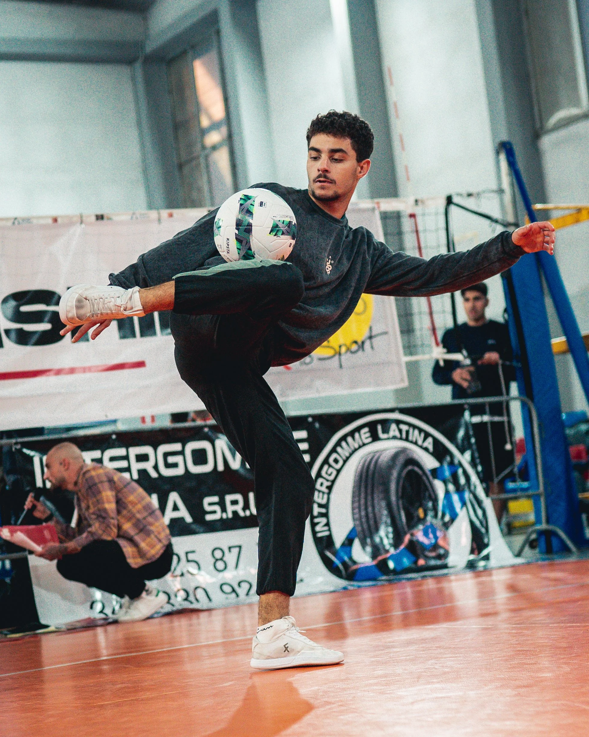 Un jeune homme joue au football en effectuant un mouvement acrobatique avec le ballon dans une salle de sport.