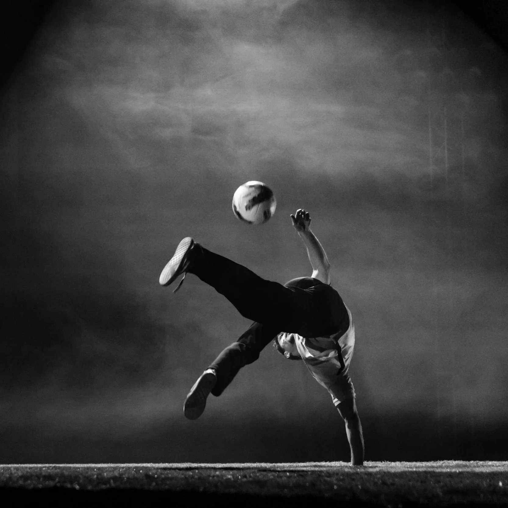 Un joueur de football effectue un flip acrobatique pour frapper le ballon lors d'un match, en noir et blanc.
