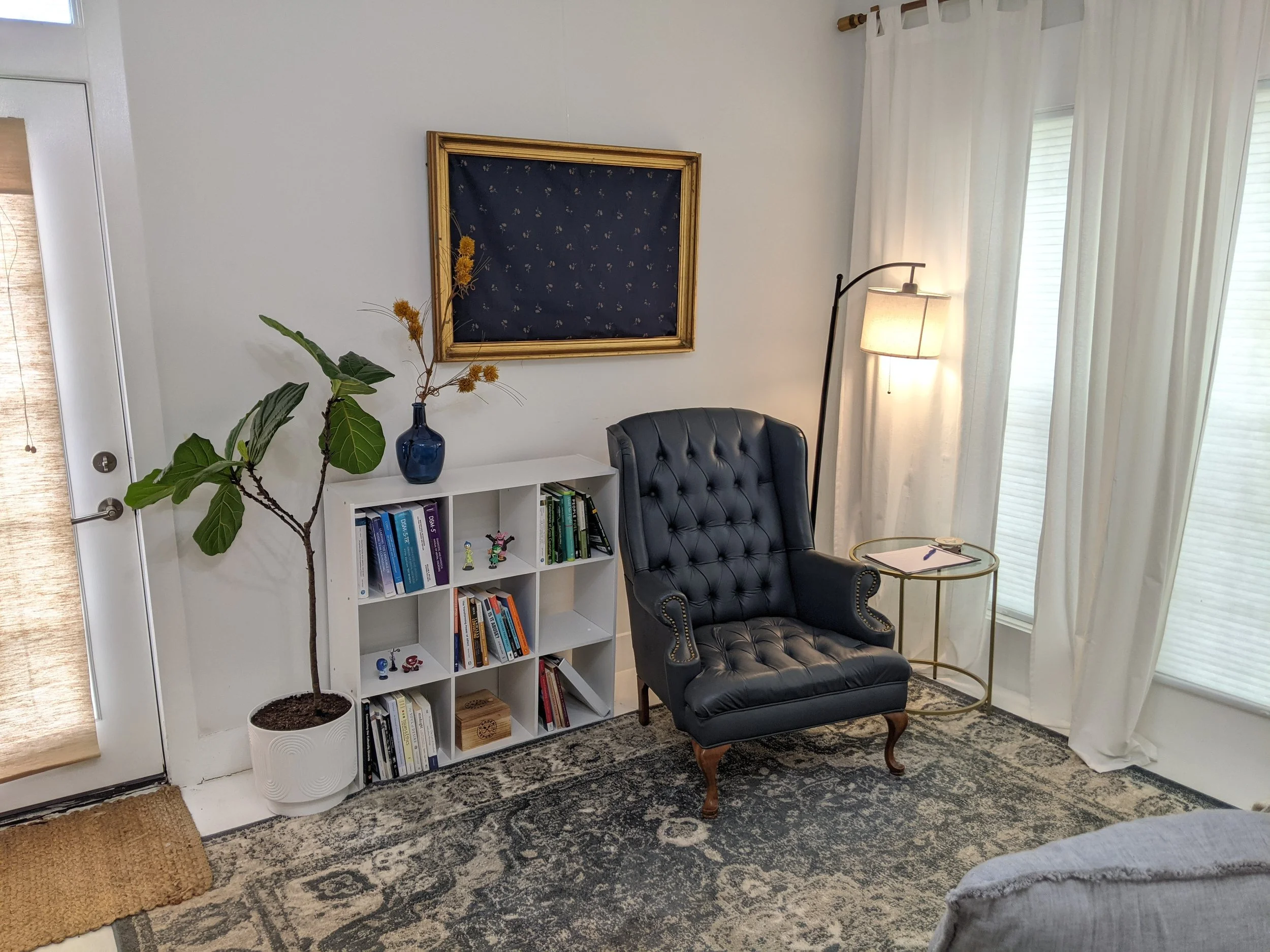 Blue chair next to bookshelf and plant with gold framed fabric in background
