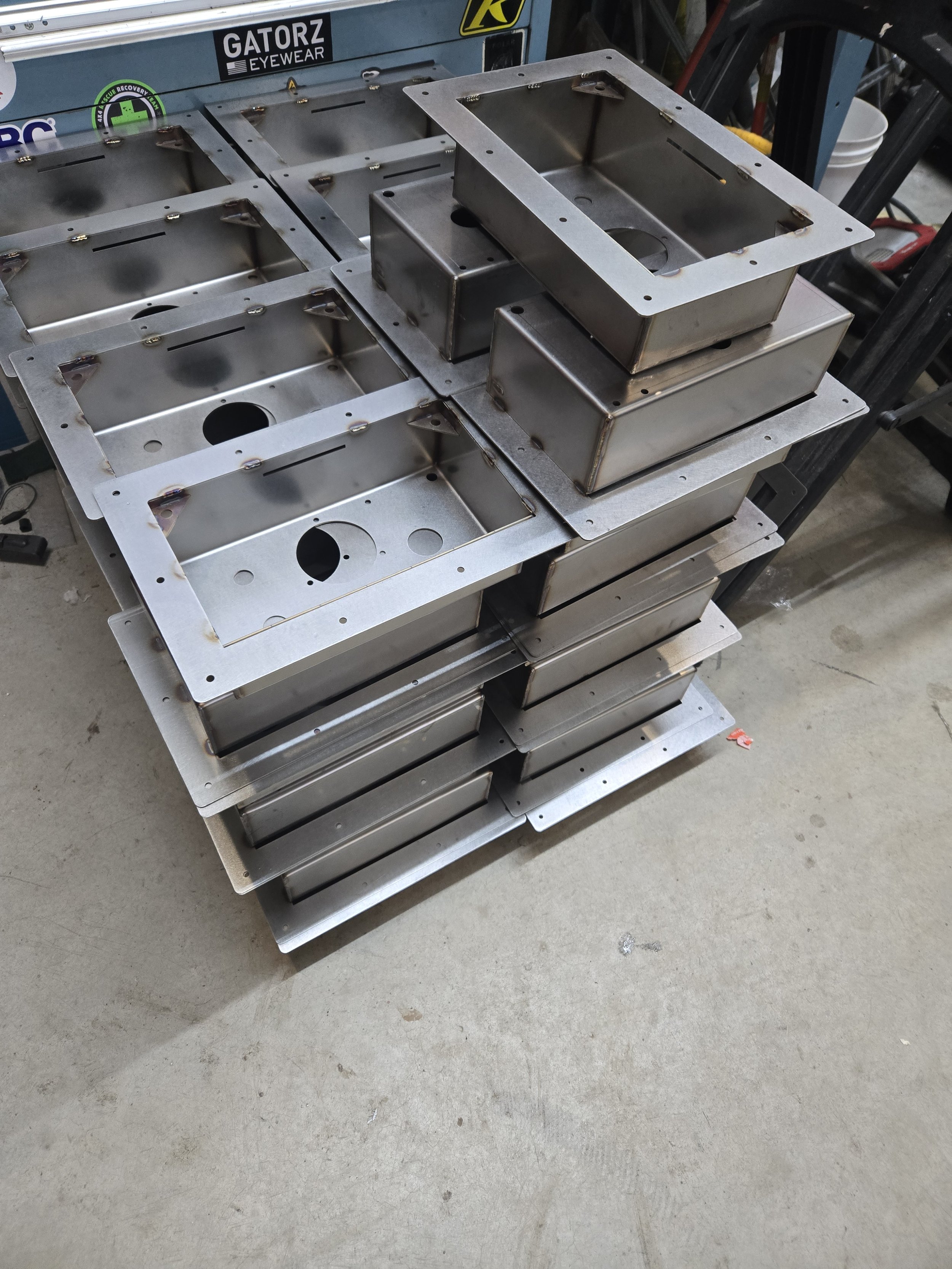 Stacked metal boxes with cutouts and mounting brackets on a workbench in a workshop.