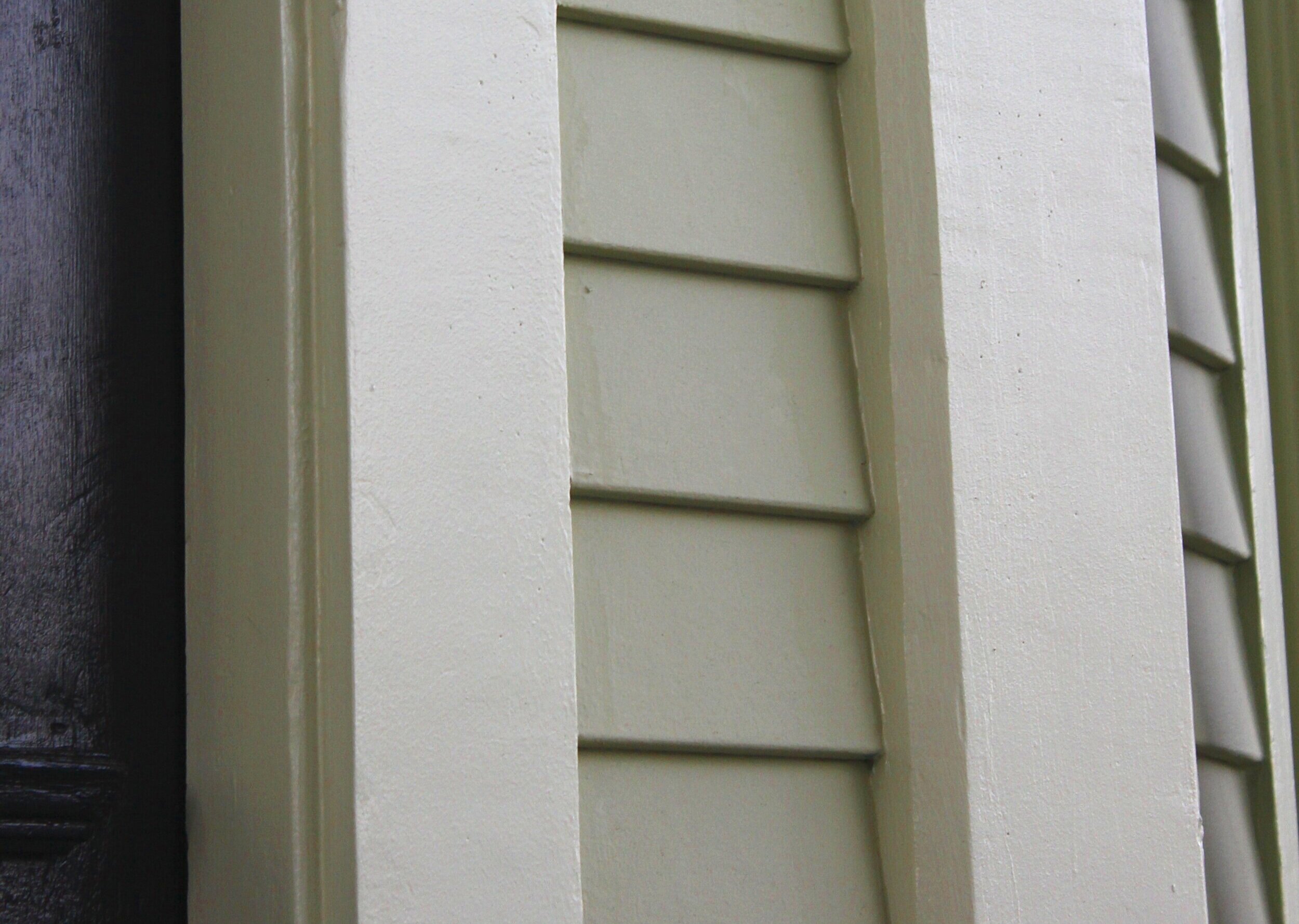 Close-up of a house corner with green siding, white trim, and black window frame.