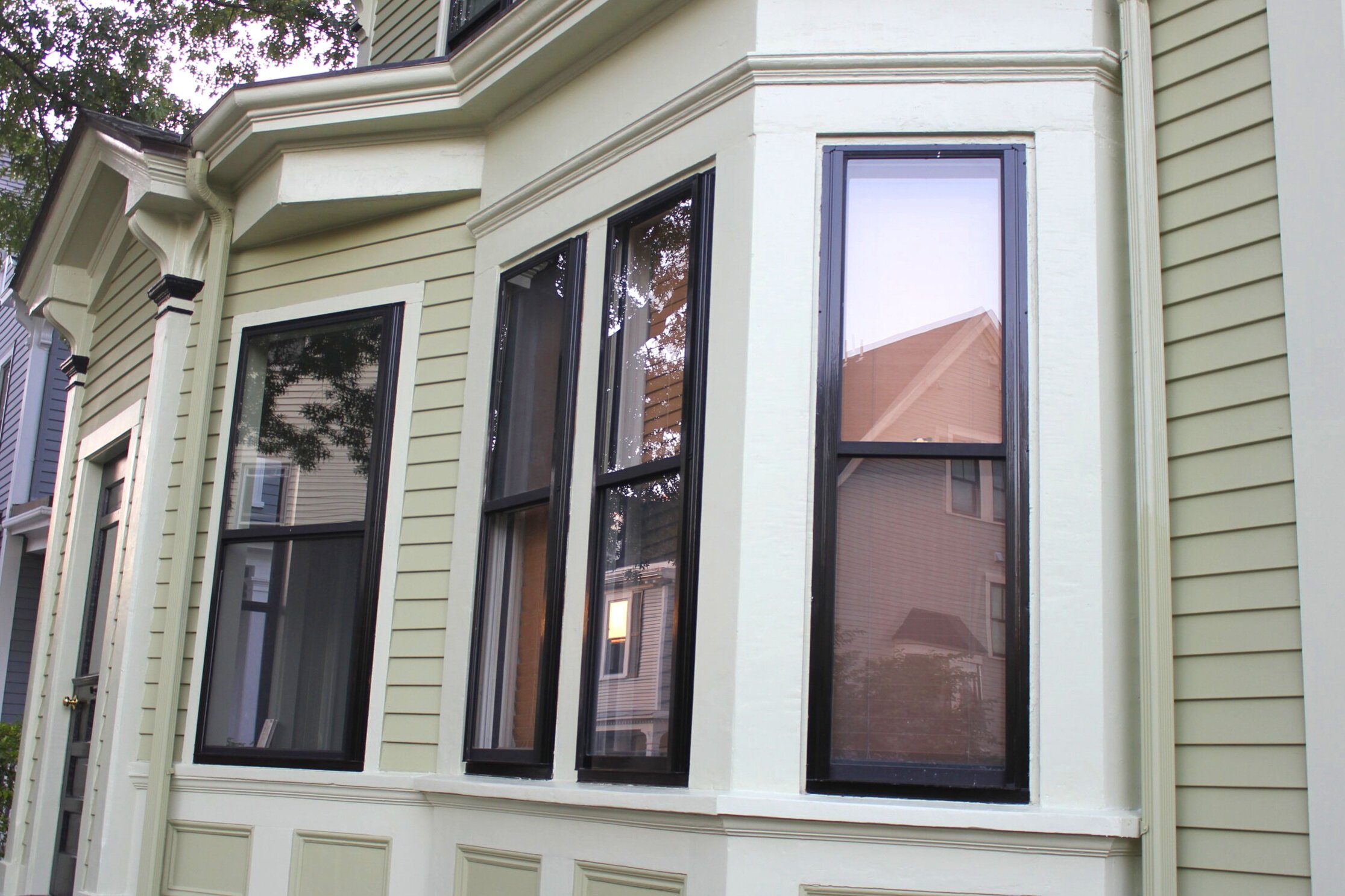 Close-up of a house's exterior bay windows and green siding, black trim around windows, and decorative molding below the windows on Custer Street, Jamaica Plain.