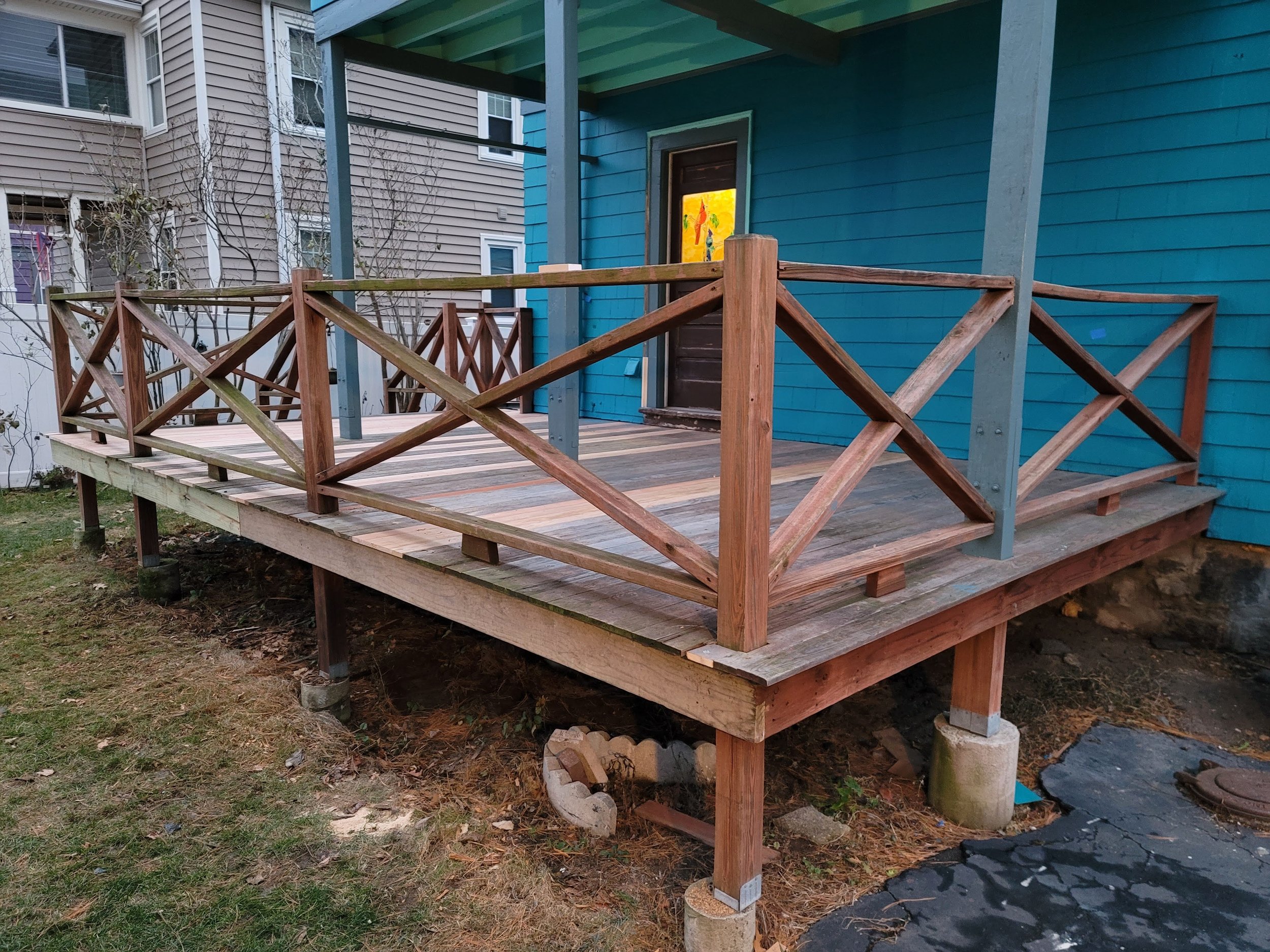 Wooden deck under construction with railings attached, existing next to a colorful blue house, in front of neighboring beige houses in Dorchester, Boston.