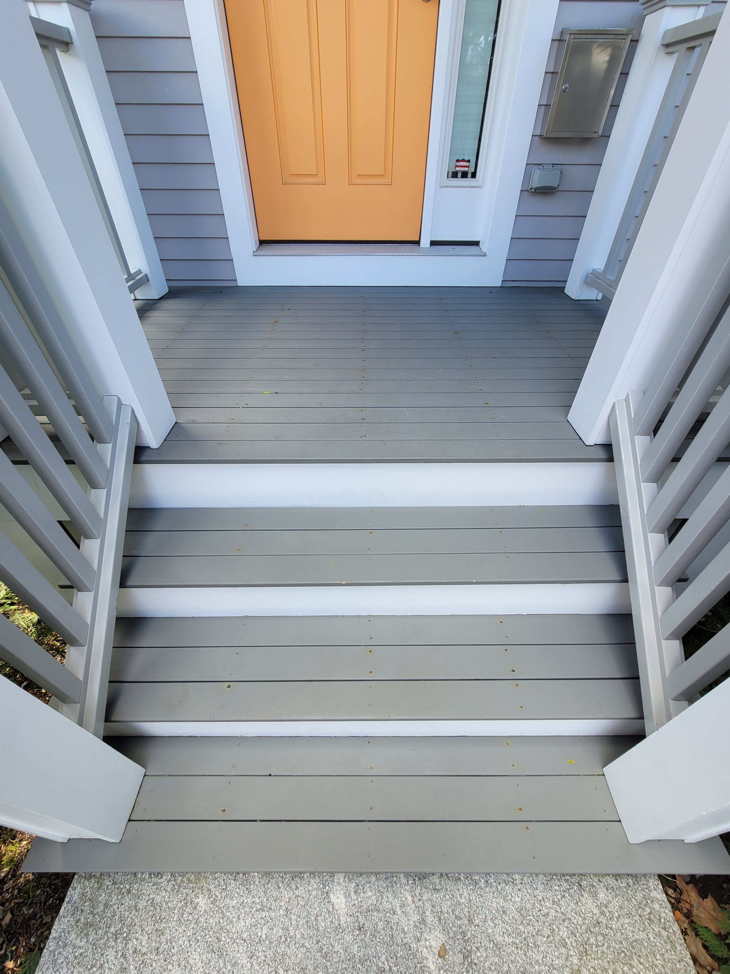 Front porch on Neponset Avenue, Roslindale with gray wooden steps that were recently painted by Ryan Painting, leading to an orange front door, white trim, and attached gray siding.