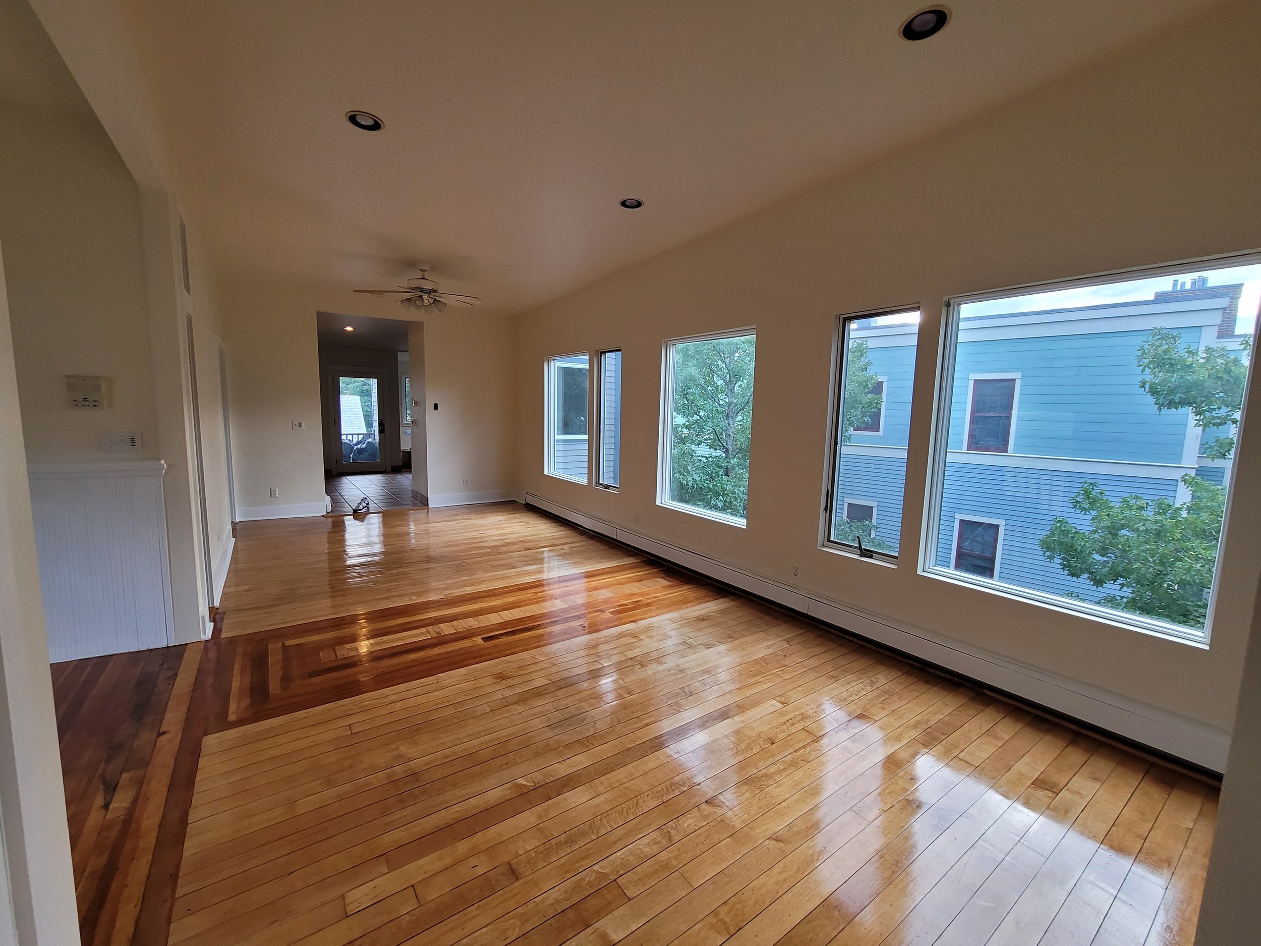 Living room with polished hardwood floors, large windows, ceiling fan, and white walls in Cambridge, Massachusetts.