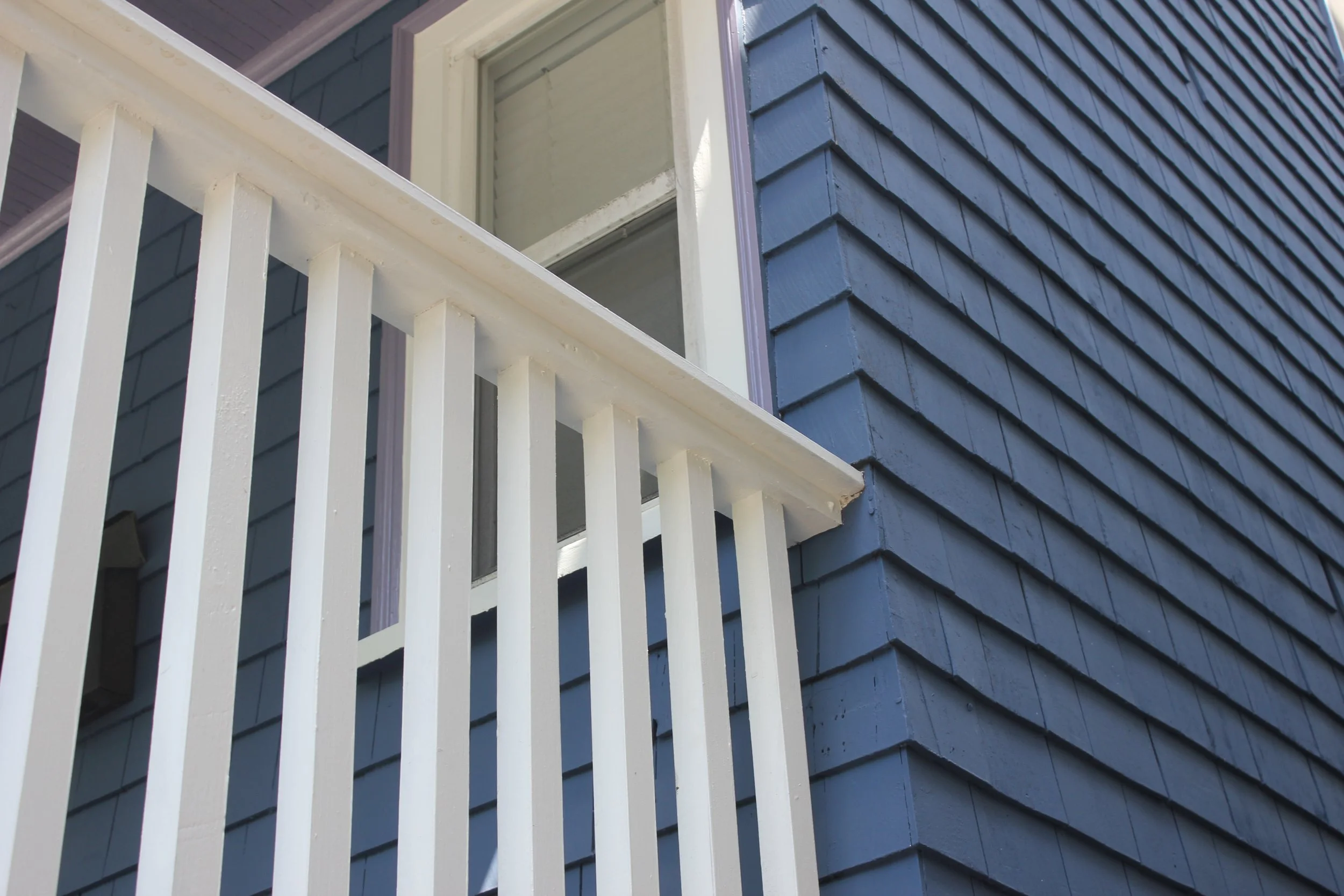 Close-up of a recently painted blue house's exterior with a white balcony railing and an open window on Forest Hills Street, Jamaica Plain.