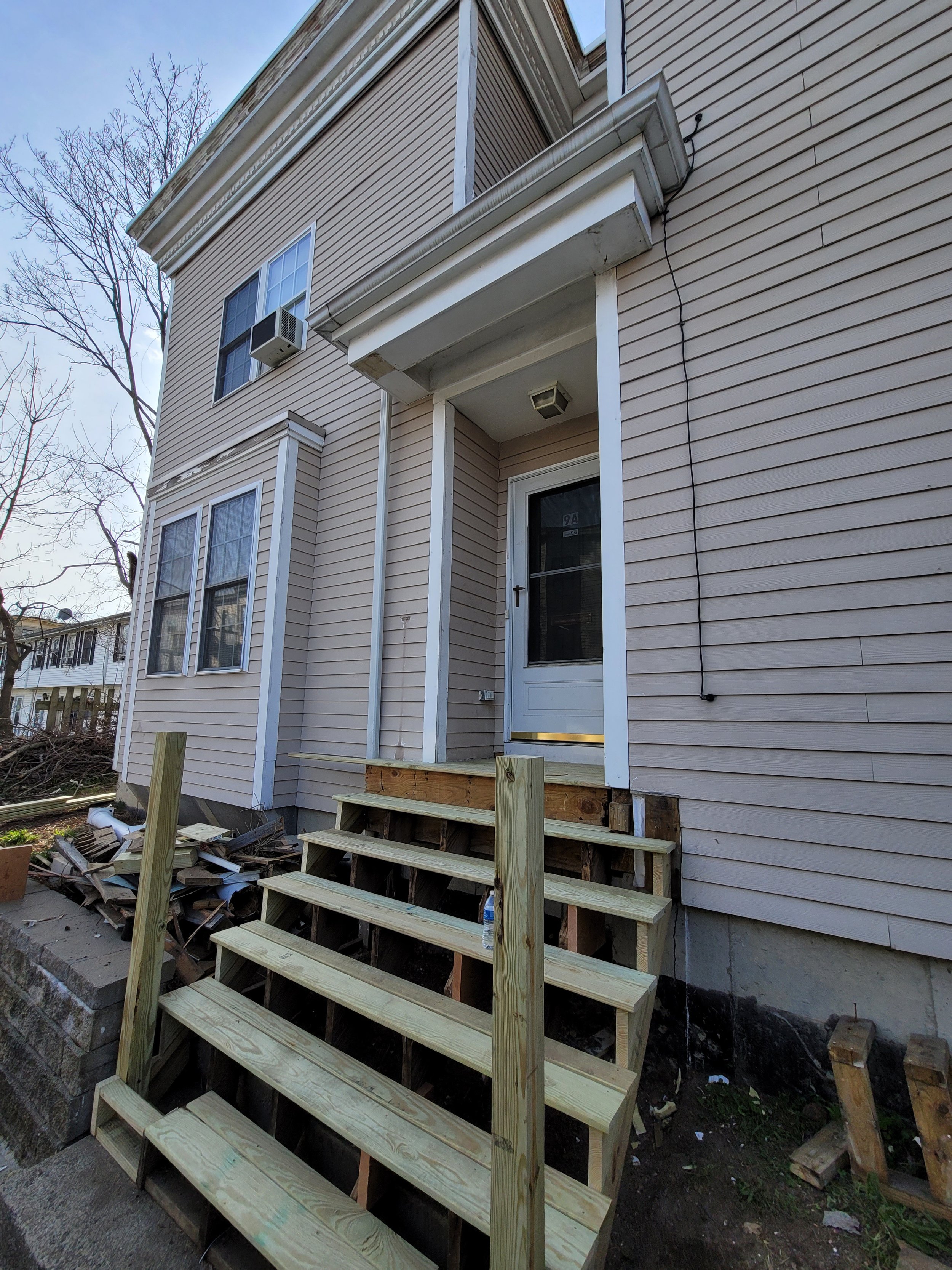 Wooden stairs under carpentry replacement by Ryan Painting outside the front door of a beige house in Roxbury, Boston.