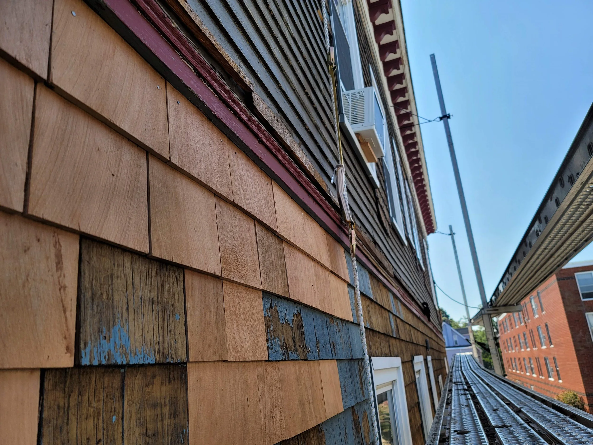 Close-up of a building in Jones Hill, Dorchester exterior with wooden shingles with expertly replaced red cedar shingles with a clear sky in the background.