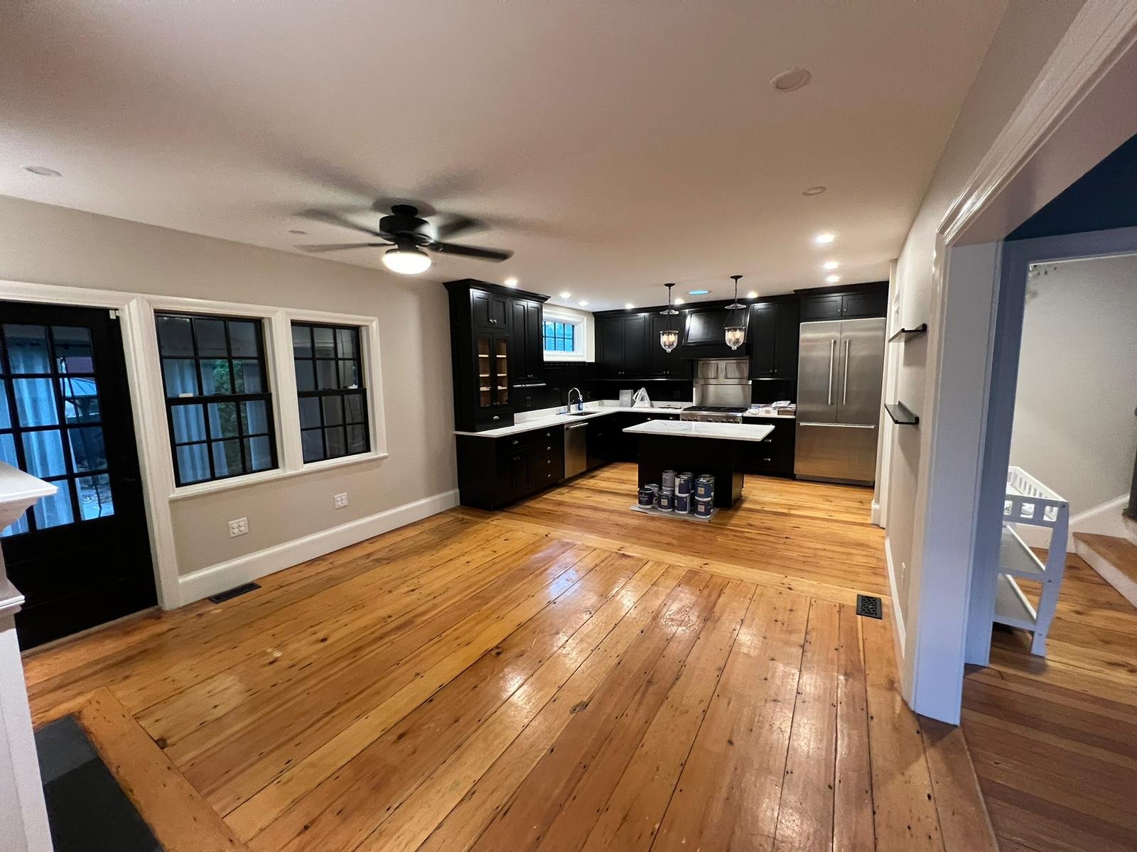 Empty kitchen with black cabinets, stainless steel appliances, a kitchen island, hardwood floors, and a ceiling fan.
