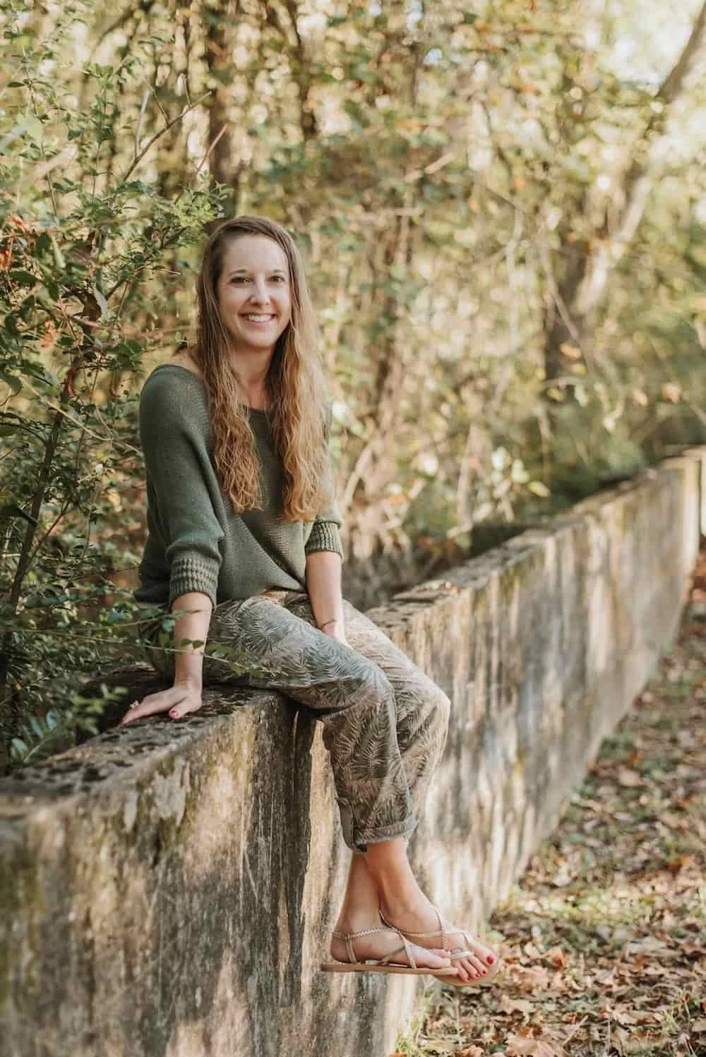 Becca Morris, Counselor and Reiki Master in Augusta, GA, sitting on a wall and leaning in with a welcoming smile.