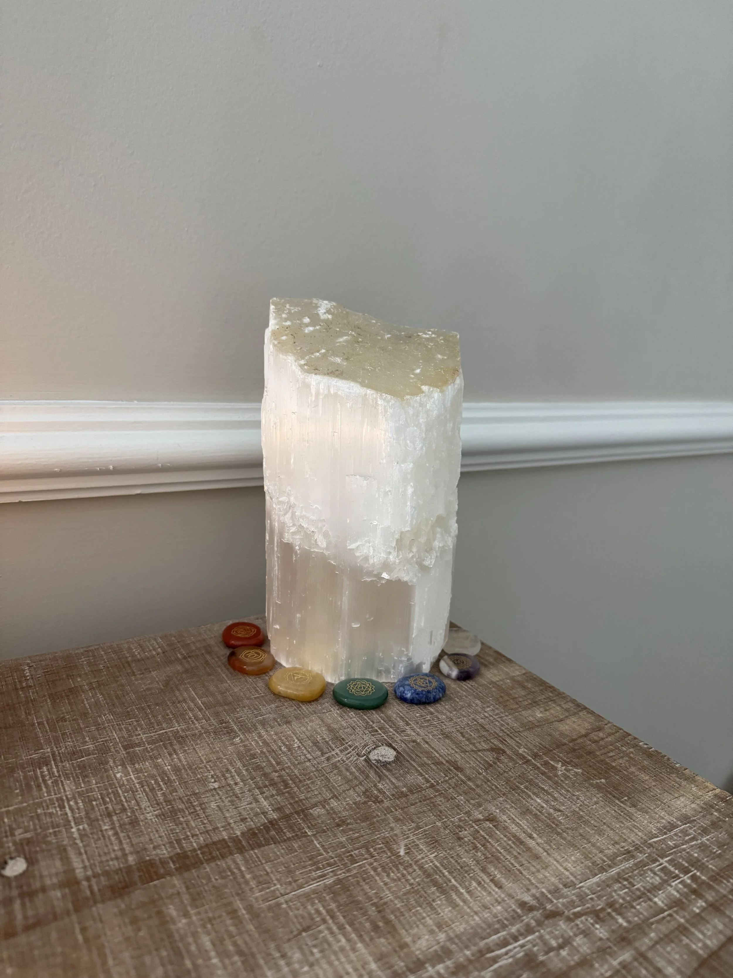 Large selenite crystal surrounded by seven chakra-colored stones for Reiki energy healing in Augusta, GA.