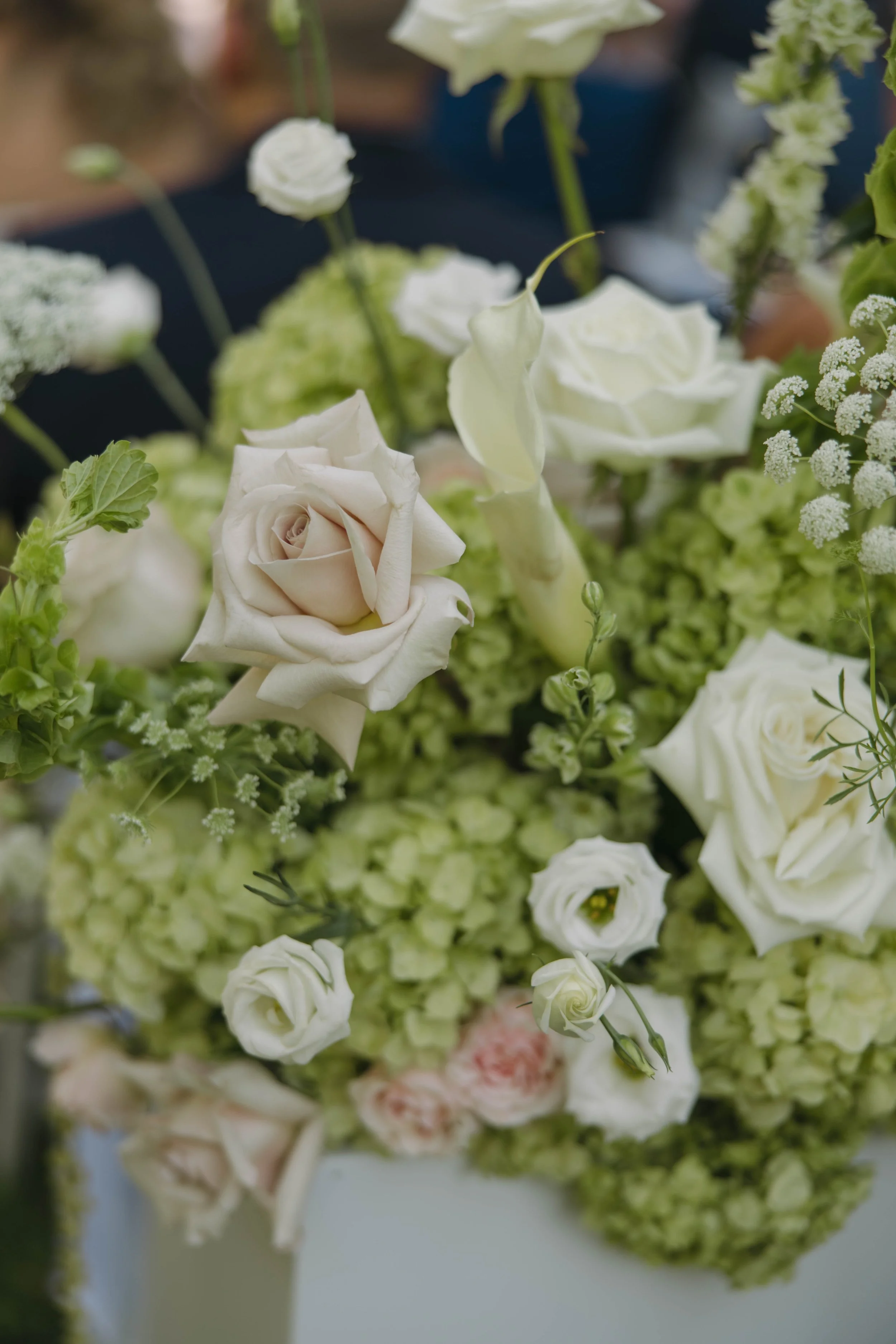 Close-up of a floral arrangement with white roses, green hydrangeas, and other white and light pink flowers.