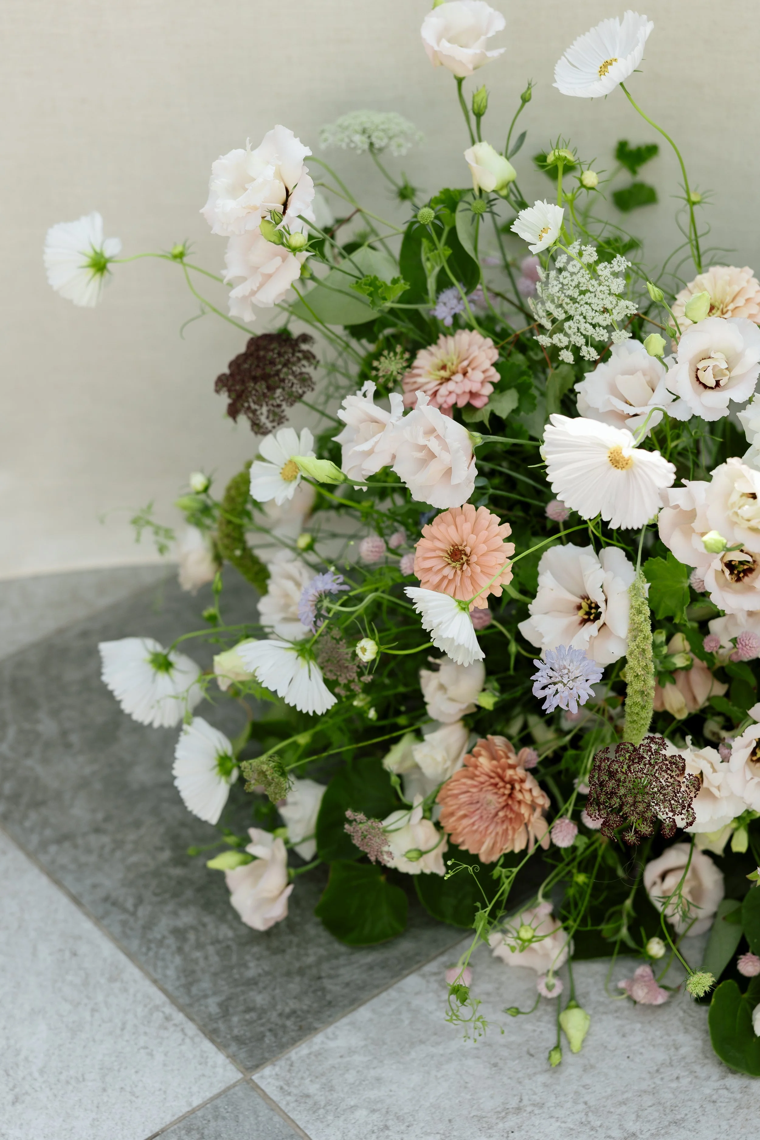 A bouquet of assorted light-colored flowers, including white, pink, and purple blooms, arranged on a gray surface.