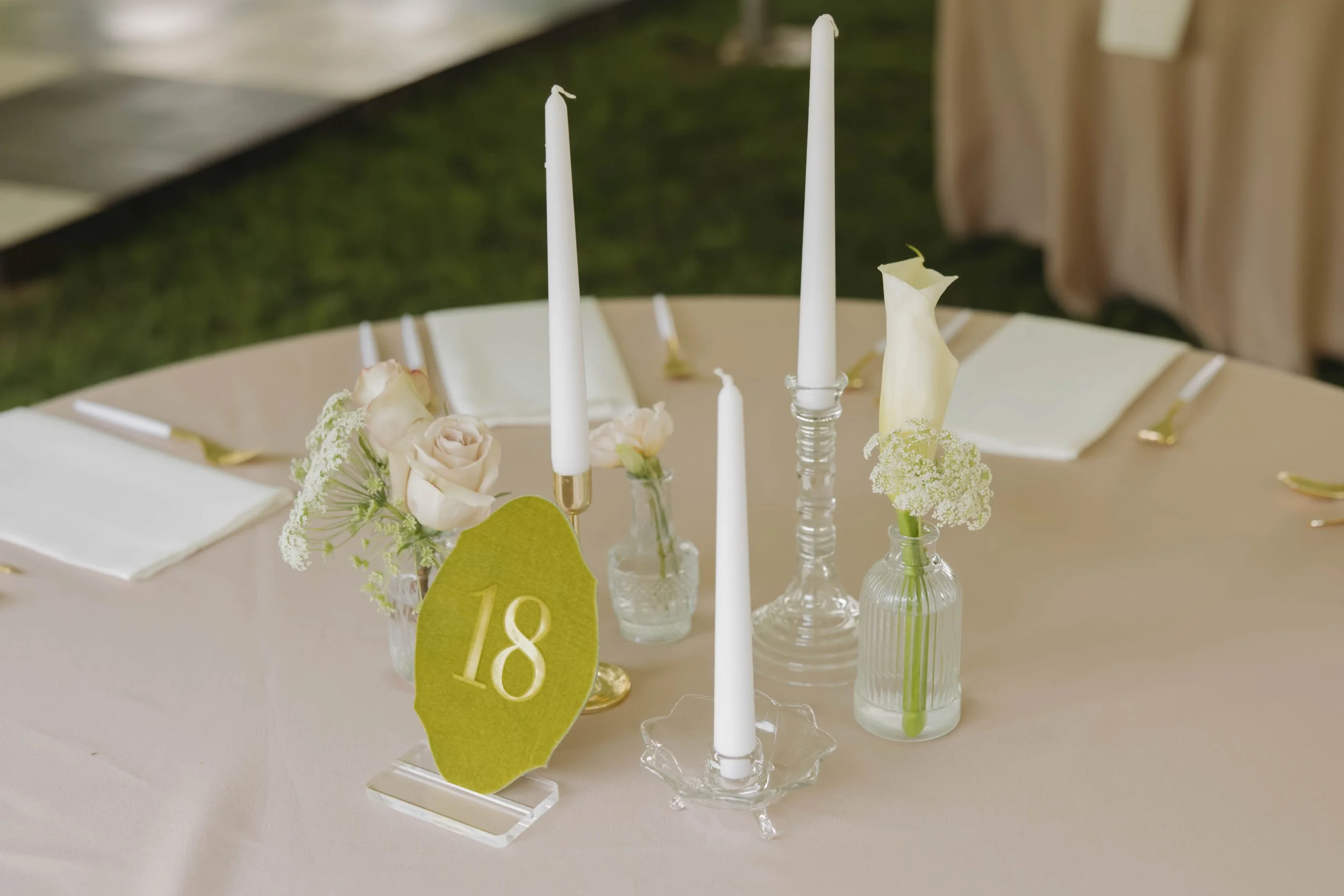 Table decorated for an event with white candles, white roses, and a table number locket marked 18