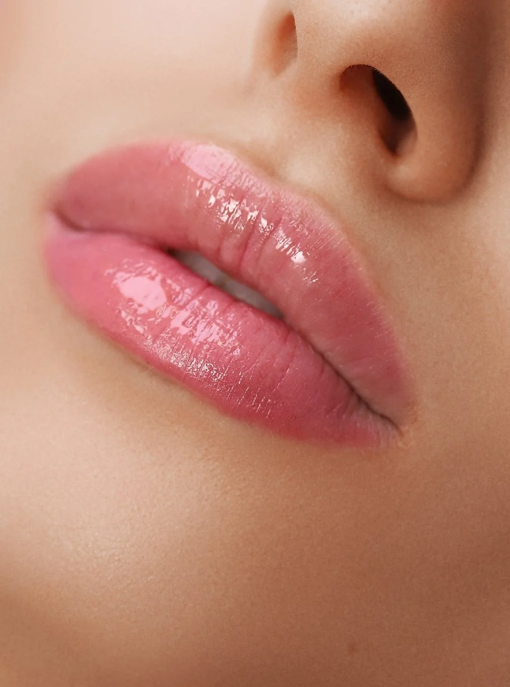 Close-up of shiny, pink lips near a person's nose.