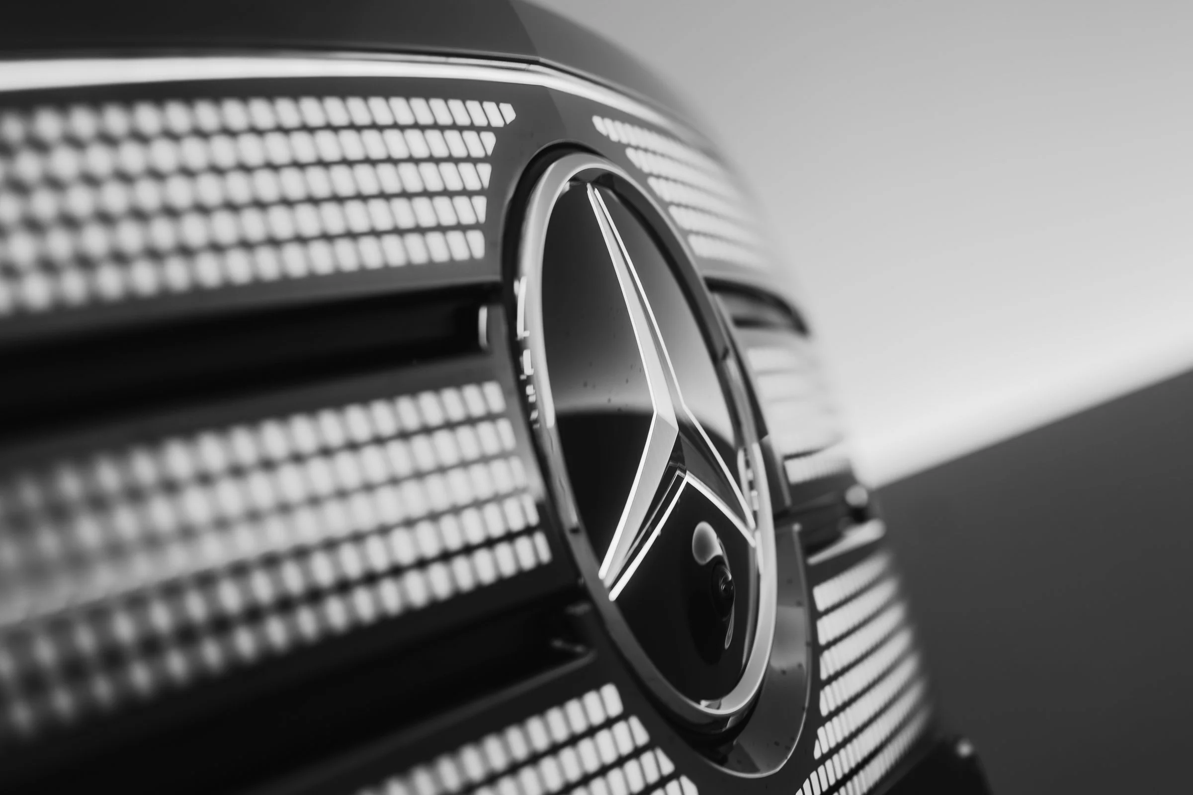 Close-up of a car emblem on a Mercedes-Benz vehicle with a focus on the star logo, surrounded by a grille with horizontal slats.