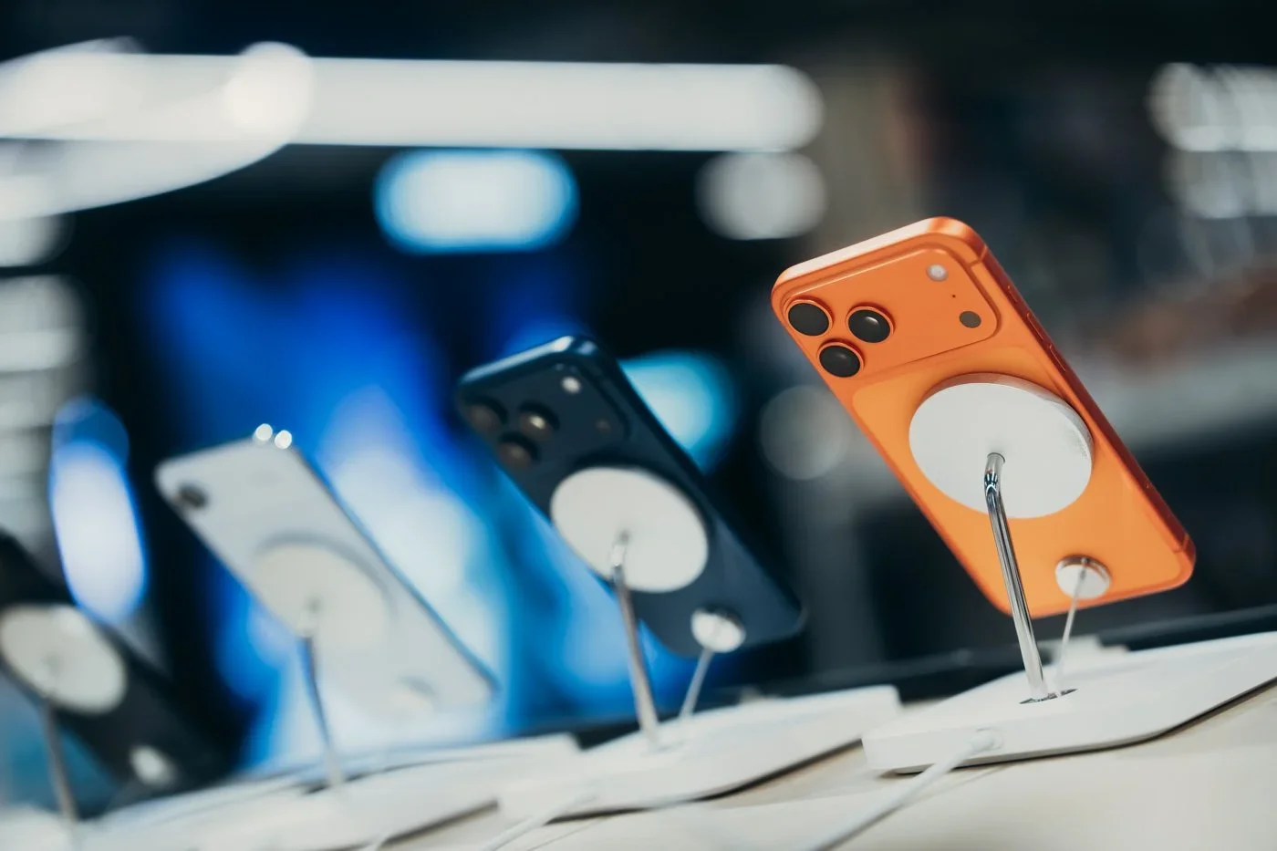 Multiple smartphones on display, secured with metal stands in a retail store, including an orange phone with a pop socket.