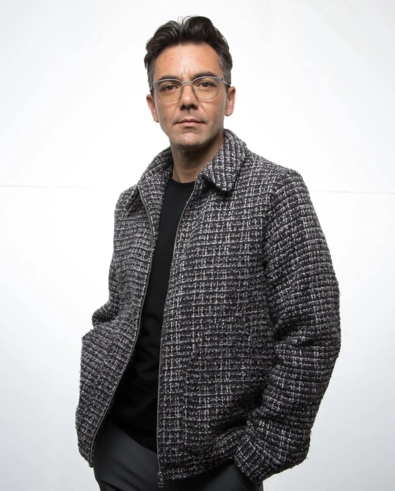 LGBTQ-affirming therapist wearing glasses, a black shirt, and checkered jacket, standing against a white background.