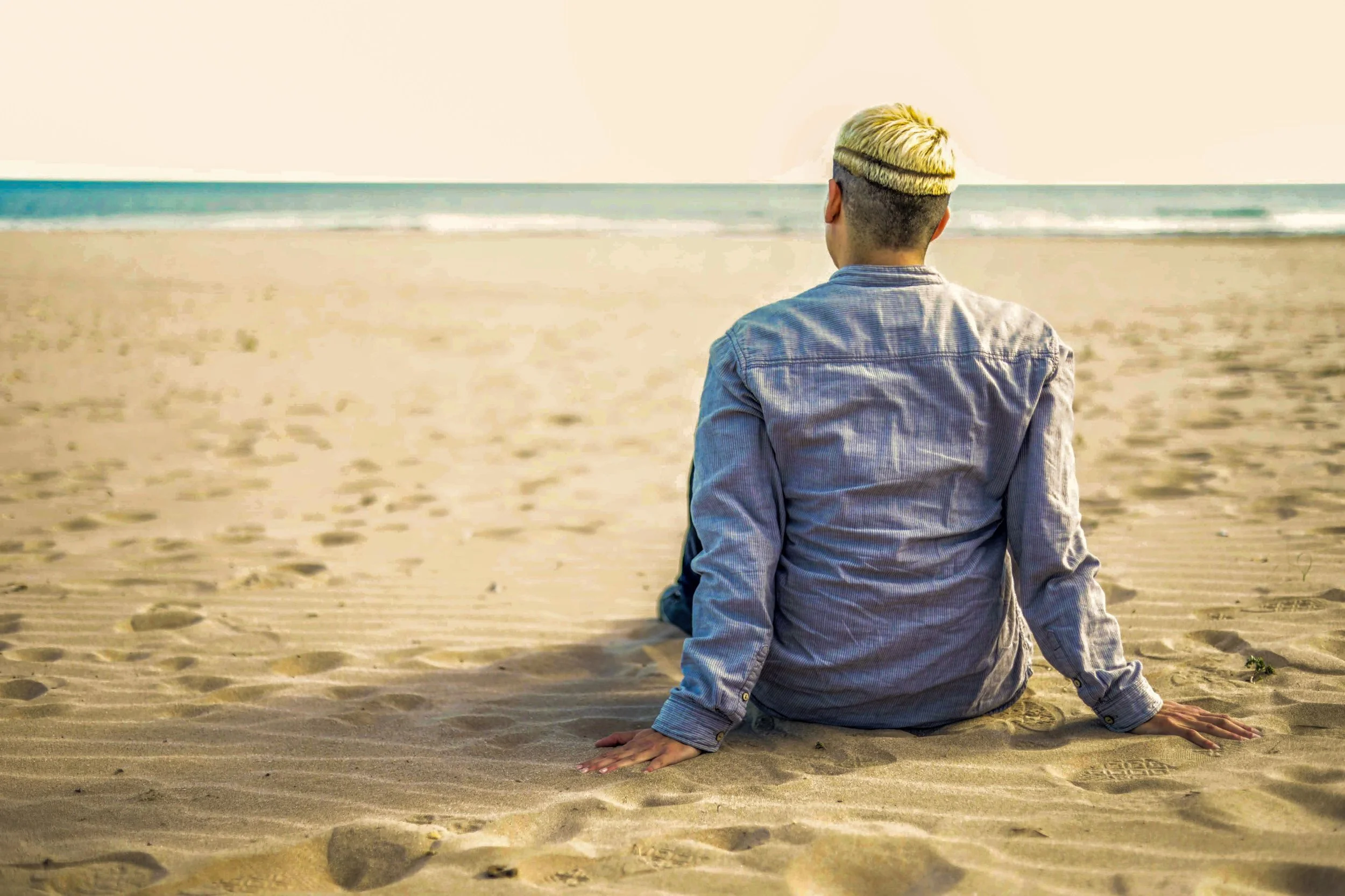 Person sitting on a sandy beach facing the ocean.